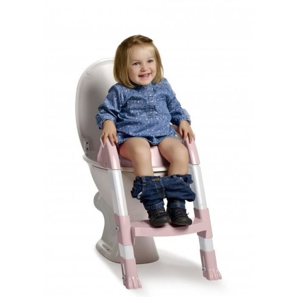Ein lächelndes Kleinkind sitzt auf einer Toilette mit einem rosa Tritthocker. Sie trägt ein blaues Kleid und Jeans, ihre Stiefel stehen auf der Stufe.