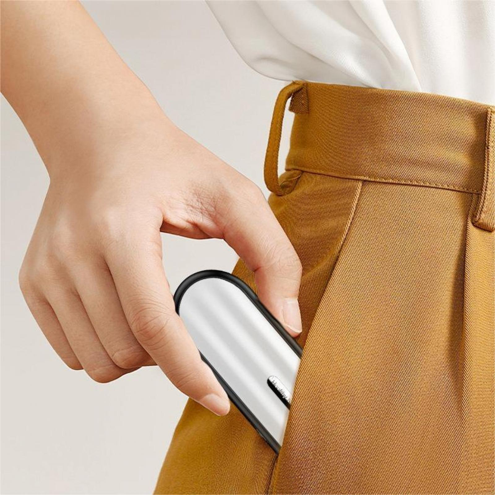 Eine Hand, die ein weißes und schwarzes Gerät in eine Tasche einer braunen Hose steckt. Ein weißes Hemd ist sichtbar.