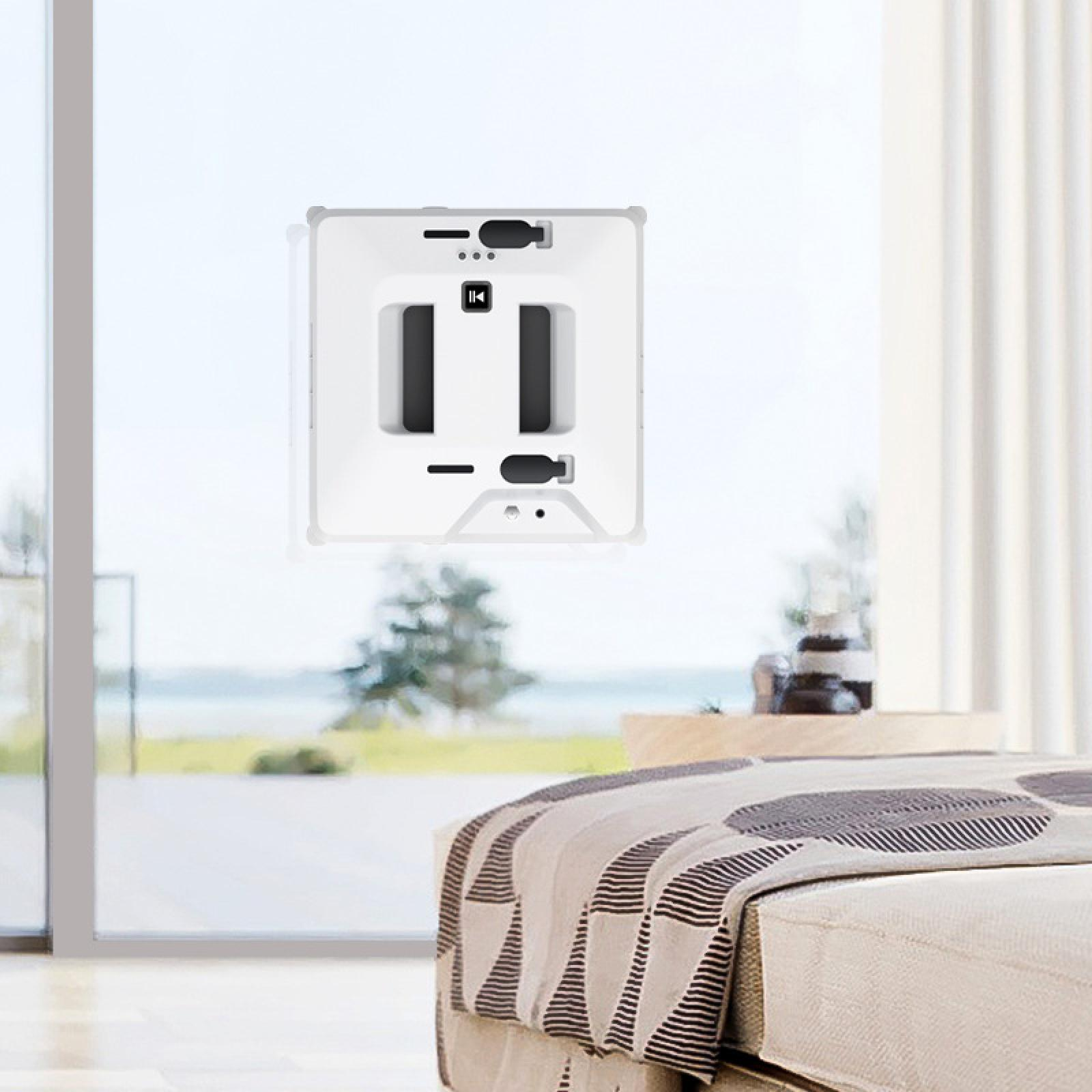 Ein weißer Fensterputzroboter befindet sich an einem Fenster. Vor dem Fenster befindet sich ein Bett. Draußen ist ein Baum zu sehen.