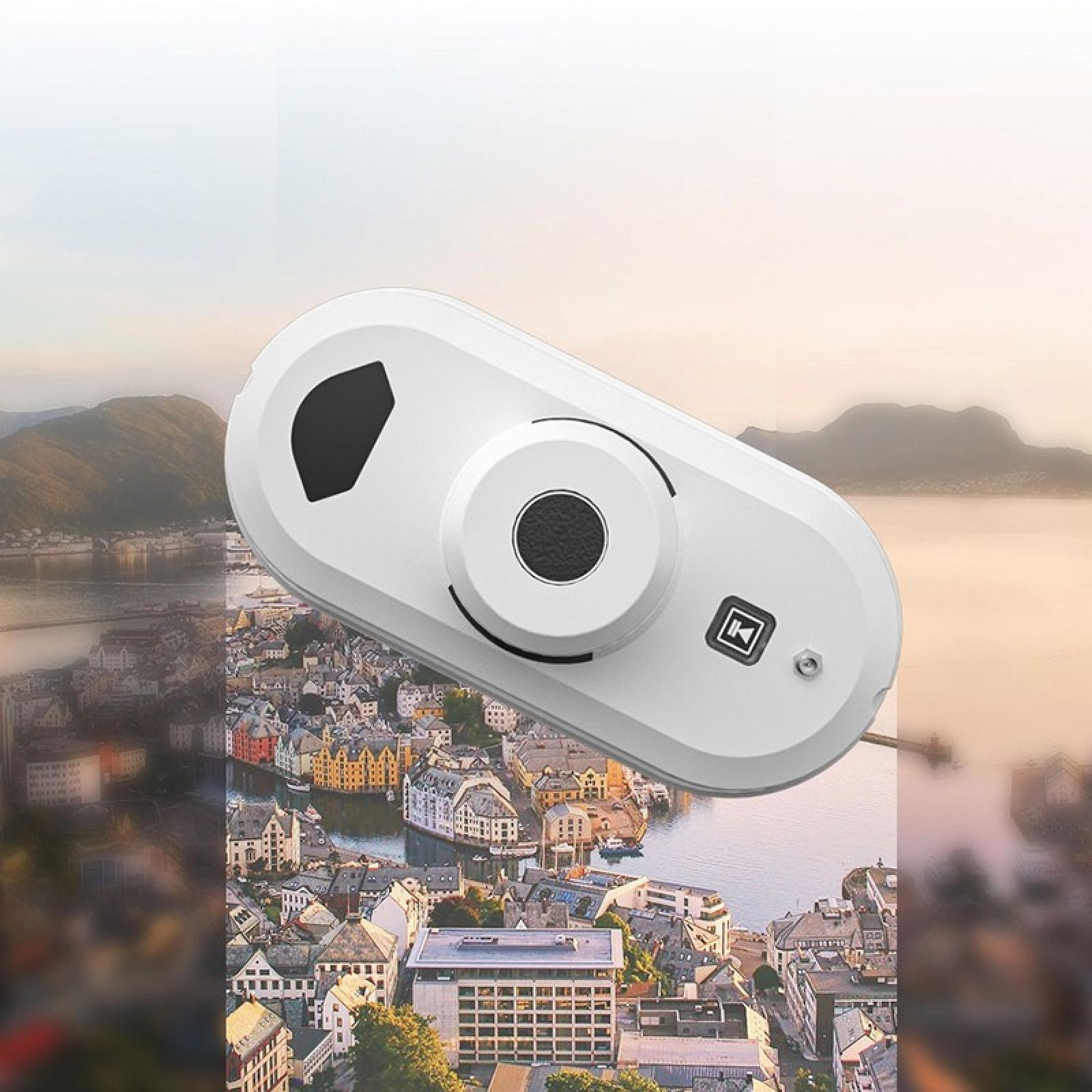 Ein weißer Fensterputzer-Roboter mit schwarzen Details über einer Stadt und Bergen.