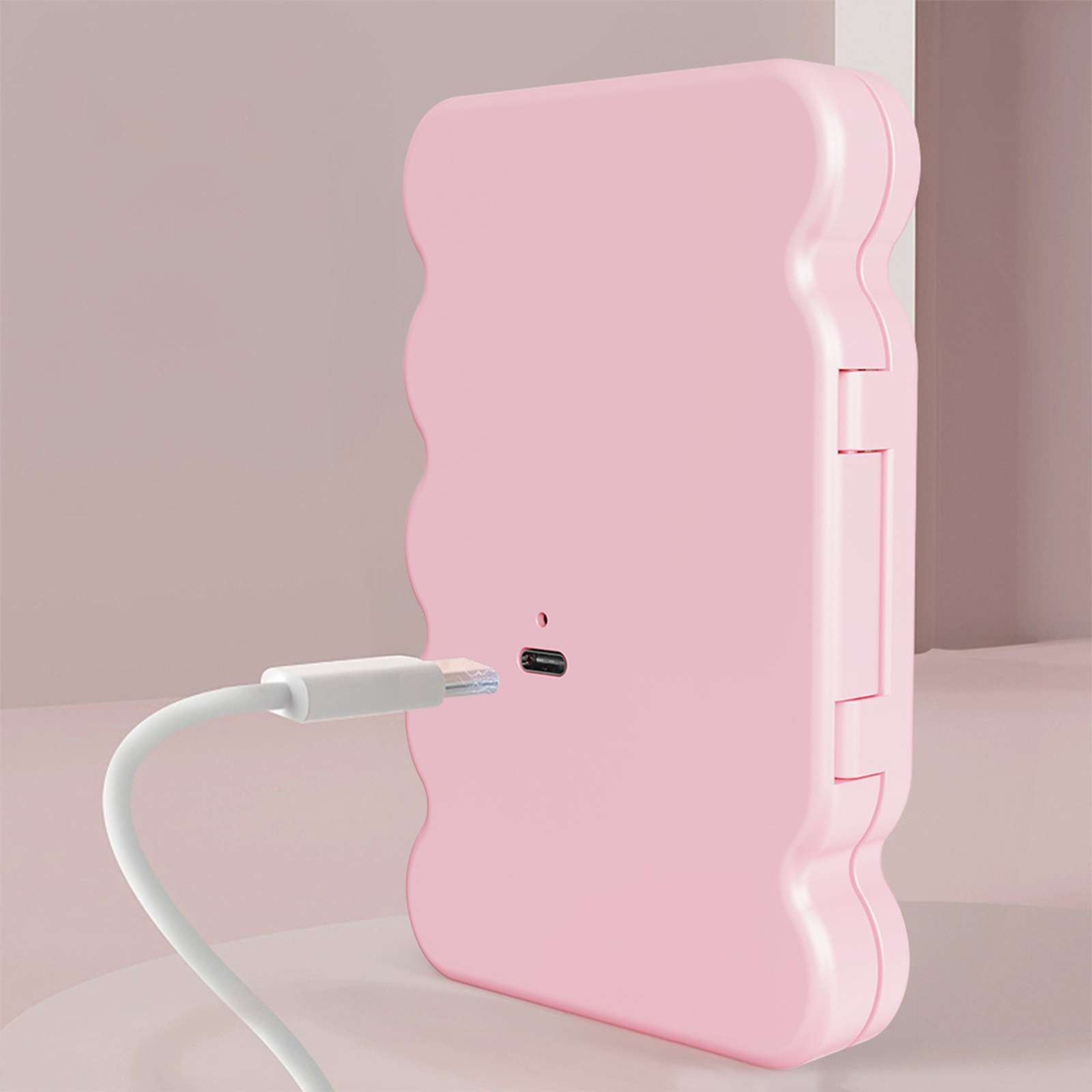 Ein rosa Gerät mit gewelltem Rand wird mit einem weißen Kabel aufgeladen. Der Hintergrund ist ein sanfter Rosaverlauf.