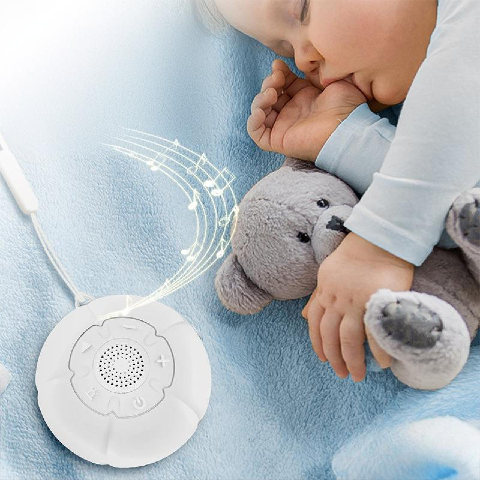 Ein Baby schläft neben einem Teddybären. Auf der Decke befindet sich ein weißes Soundgerät mit Noten.
