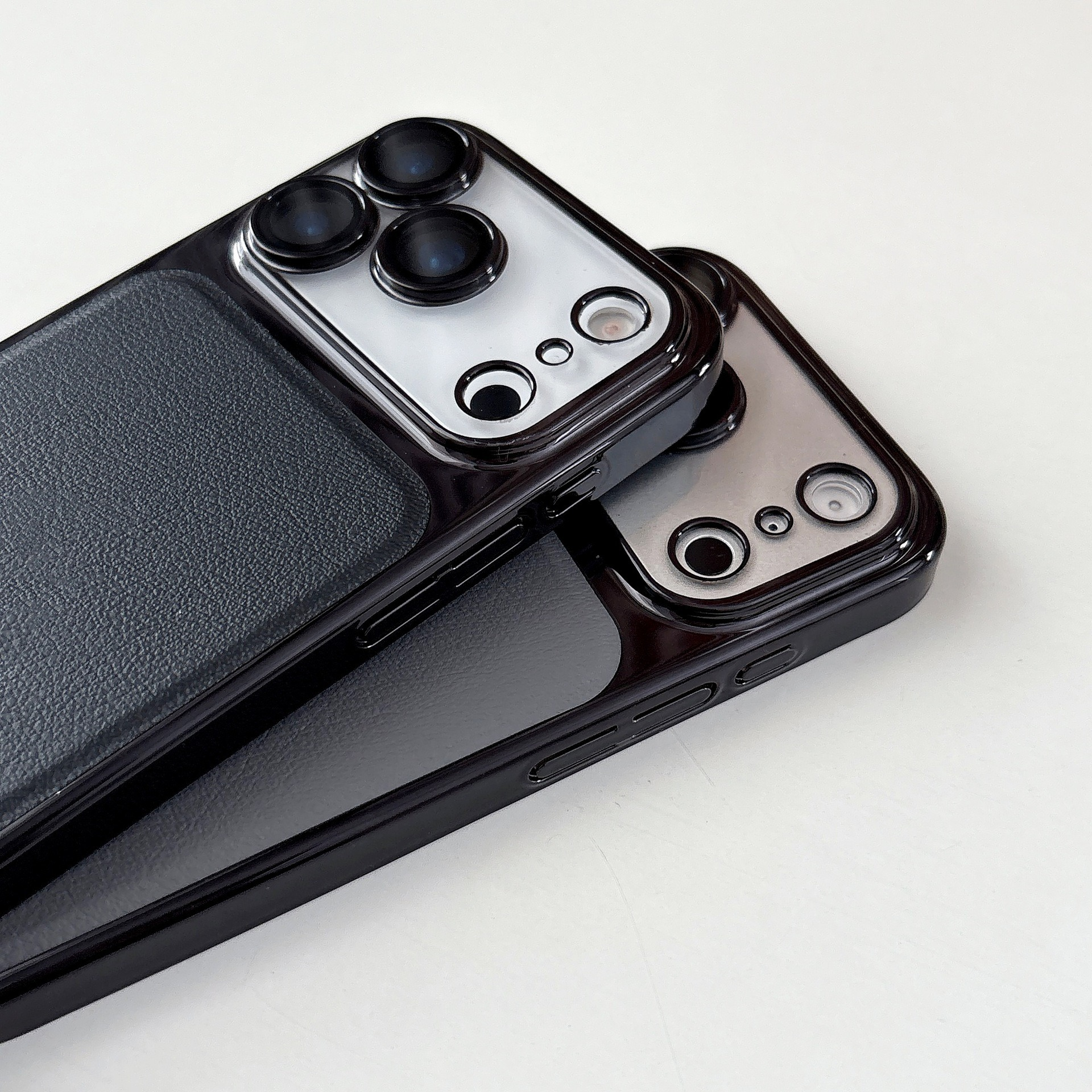 Due custodie nere per telefono con lenti della fotocamera, impilate su una superficie bianca. Una ha il retro grigio scuro.