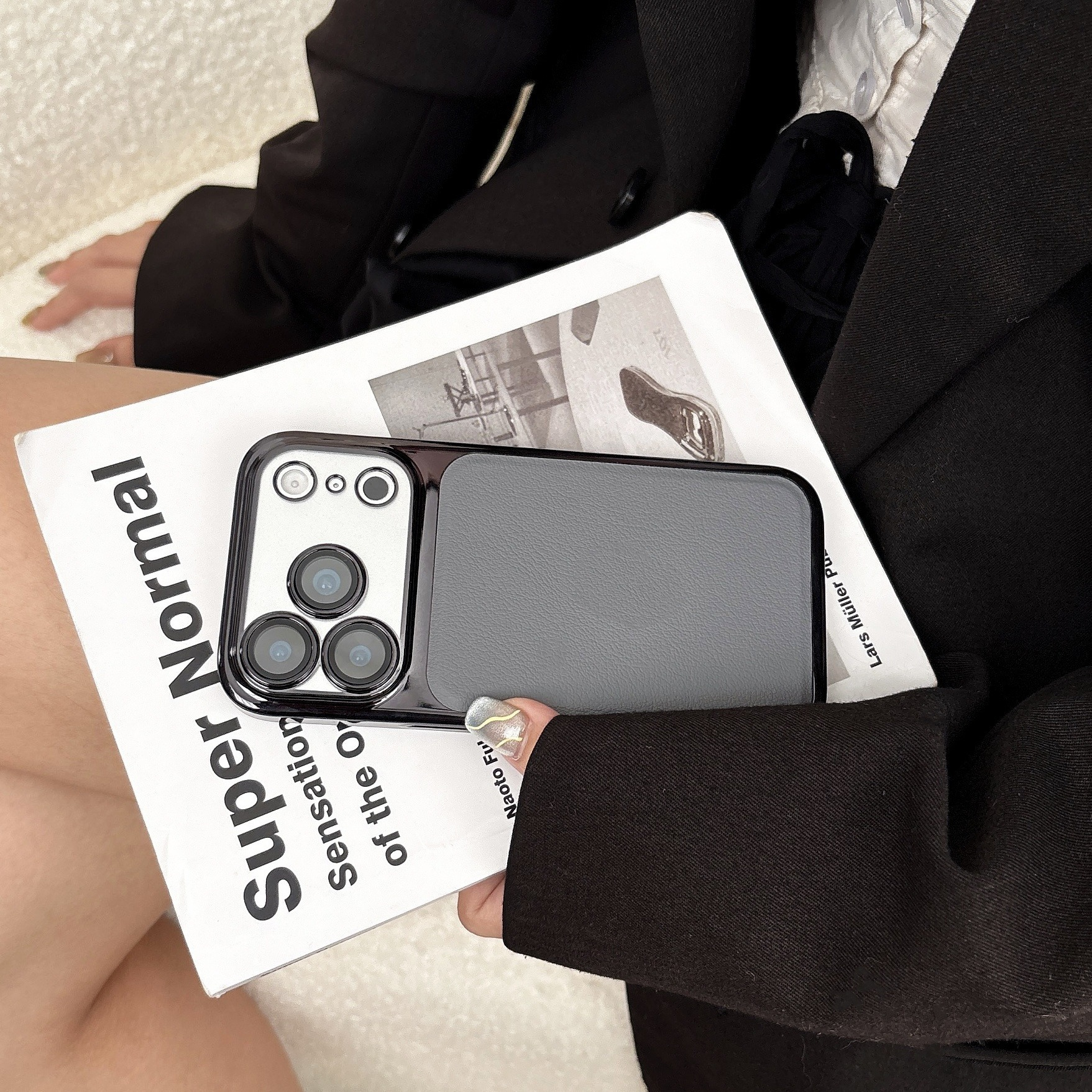 Eine Person hält eine Handyhülle mit Kameramodul. Es liegt auf einem Buch. Die Person trägt einen schwarzen Blazer.