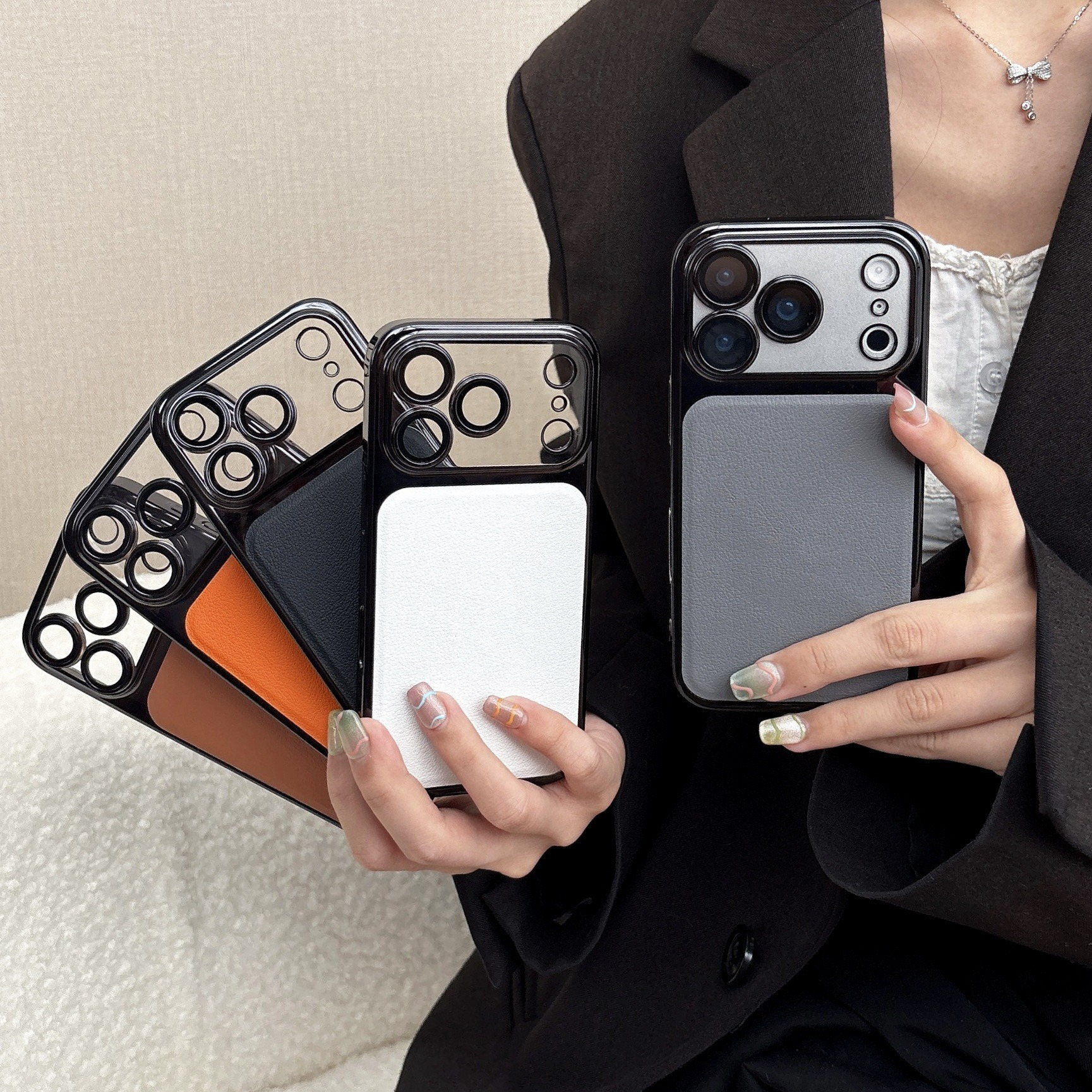 Una persona tiene in mano diverse custodie per telefoni di diversi colori: bianco, nero, arancione e grigio. La persona indossa un blazer nero.