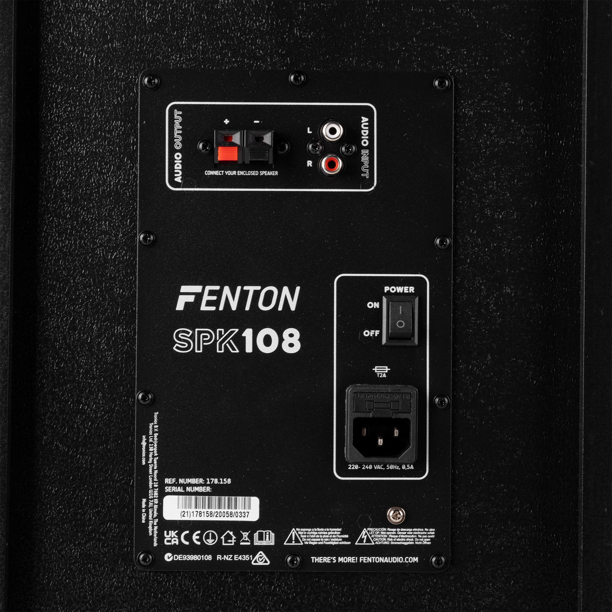 Panel trasero de altavoz negro con entradas, interruptor de encendido y la marca FENTON SPK108. Incluye etiquetas de advertencia y números de serie.