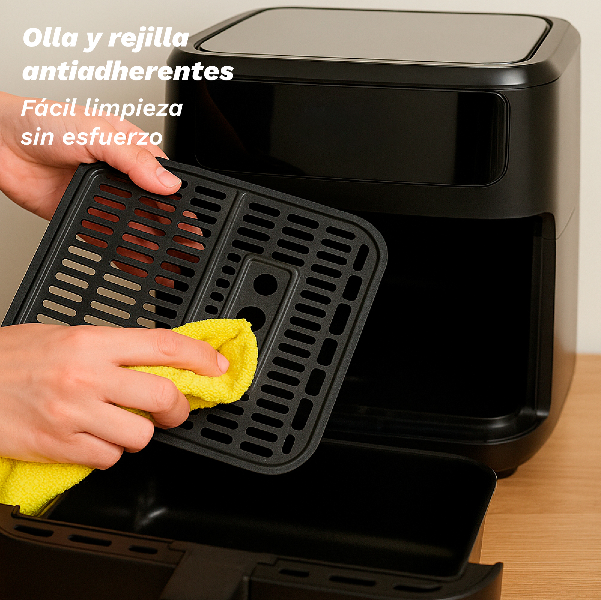 Una persona limpia una bandeja negra de freidora de aire con un paño amarillo. La freidora es negra y el fondo neutro.