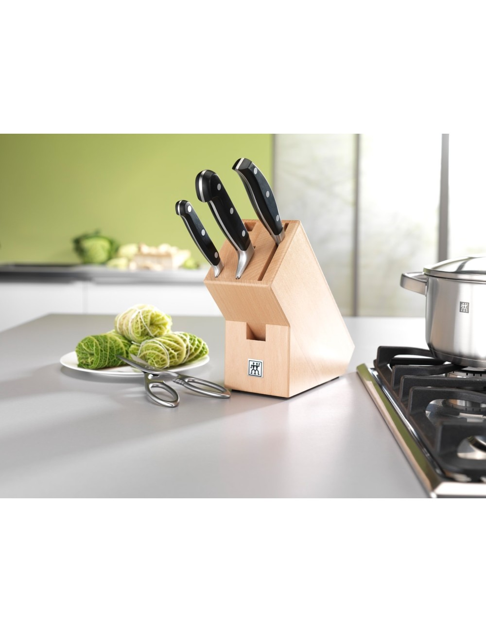 Noże w drewnianym bloku, gołąbki na talerzu, nożyczki i garnek na kuchence. Otoczenie kuchni.