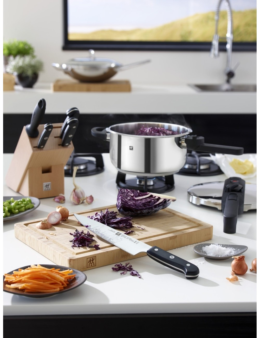 Scena kuchenna z warzywami, nożami i garnkiem. Marchew, kapusta i cebula leżą na blacie. Nóż spoczywa na desce do krojenia.