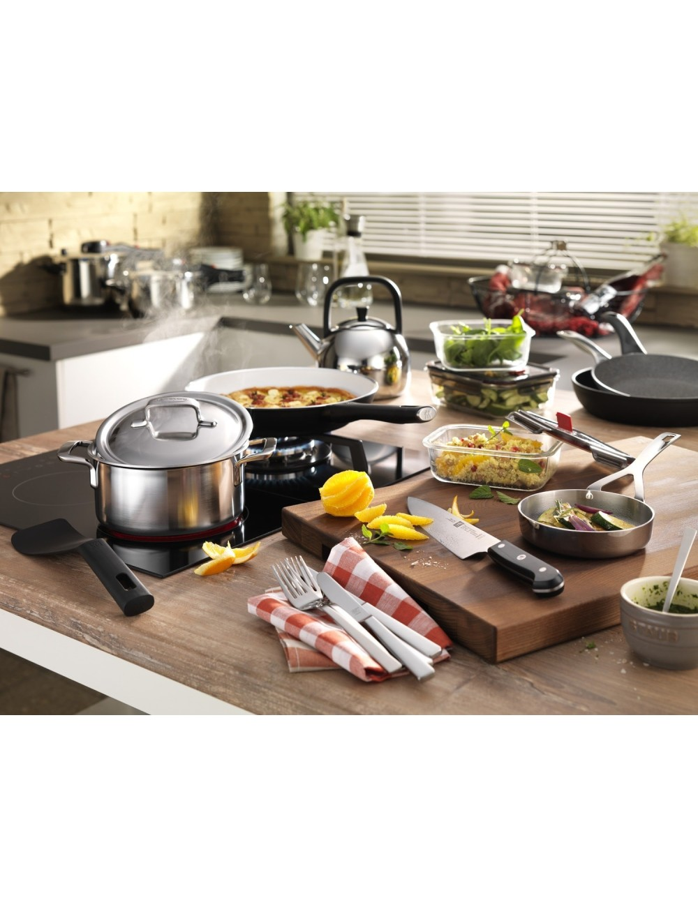 Scena kuchenna z różnymi narzędziami kuchennymi i jedzeniem. Garnki ze stali nierdzewnej, patelnie, czajnik, deski do krojenia i pojemniki na żywność.