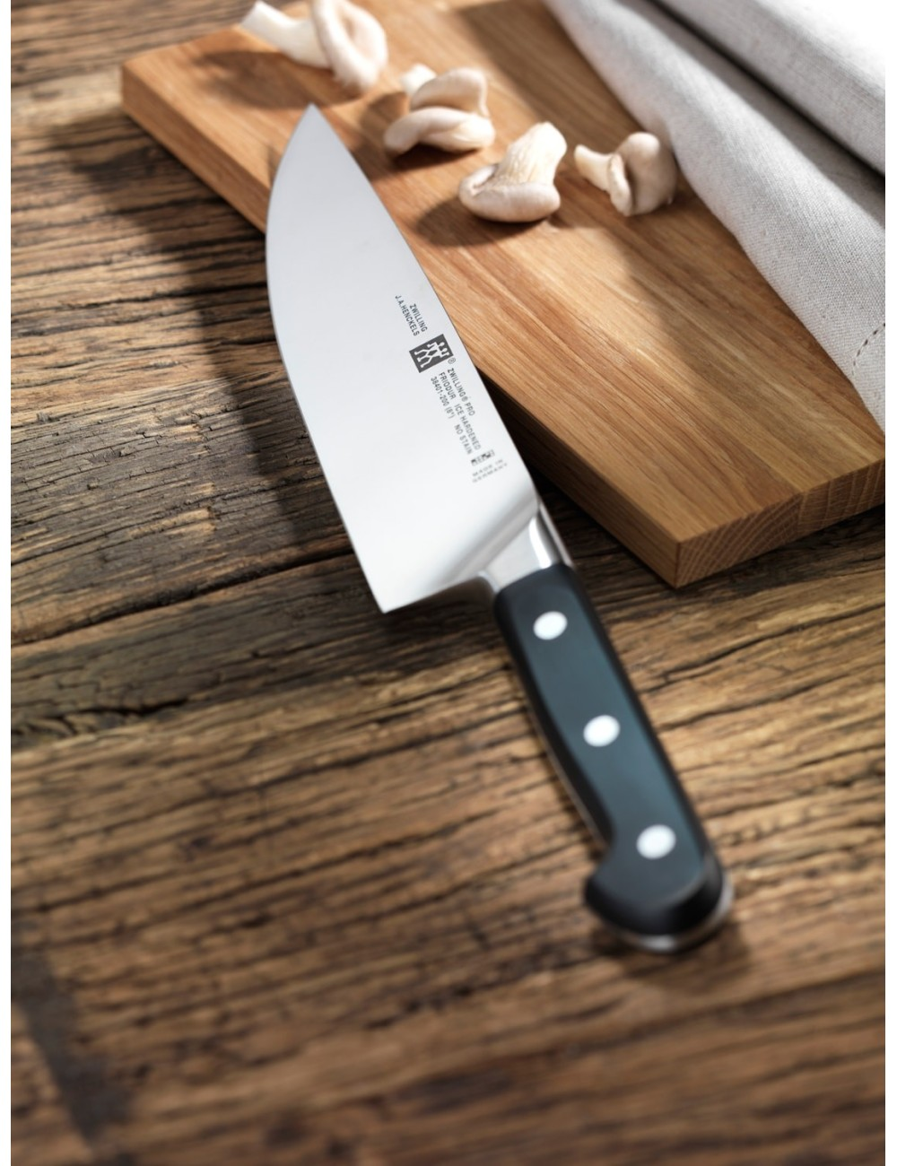 Nóż kuchenny leży na drewnianej desce do krojenia z grzybami. Rękojeść jest czarna, a ostrze srebrne. Tło to drewniany stół.