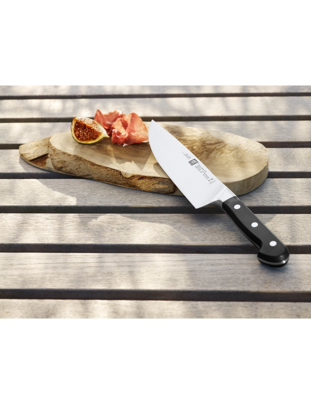 Nóż na drewnianej desce z figami i szynką parmeńską na drewnianym stole. Rękojeść noża jest czarna.