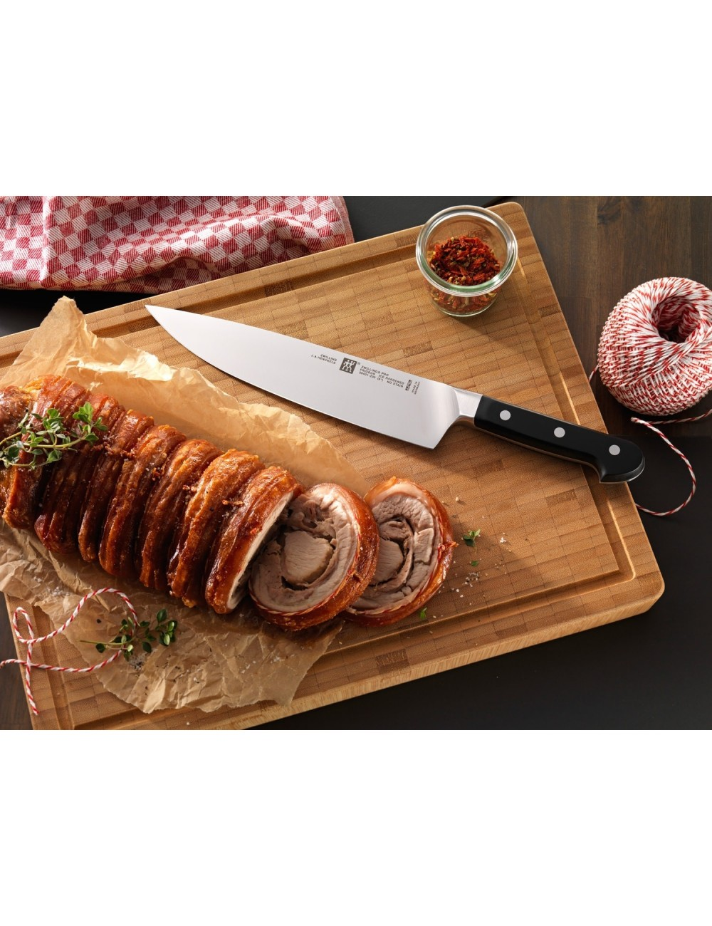 Ugotowana i pokrojona rolada mięsna z nożem na drewnianej desce, z przyprawami i sznurkiem w tle.