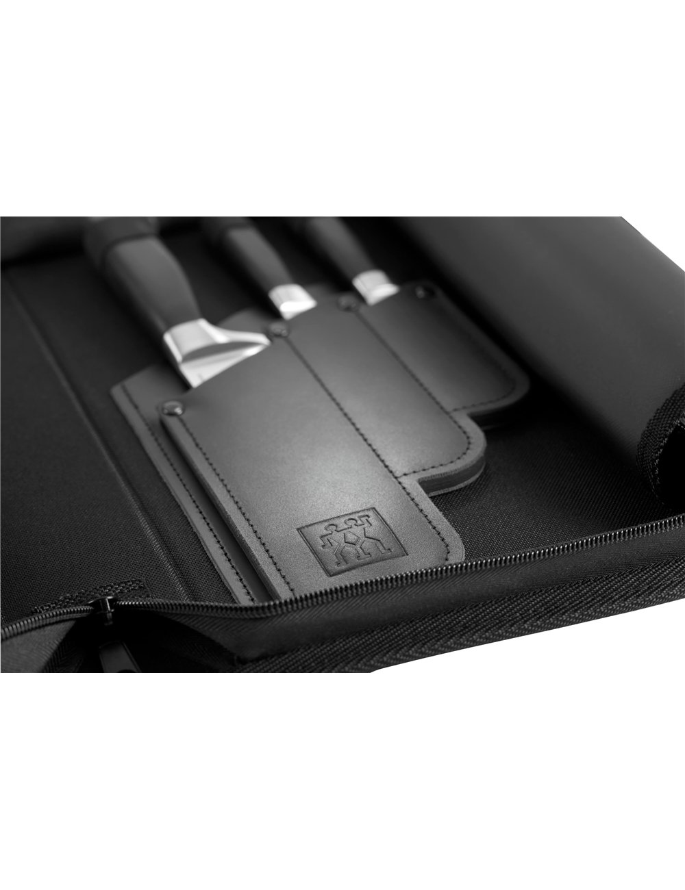 Zbliżenie czarnego zestawu noży w czarnym etui. Widoczne noże, ze srebrnymi ostrzami i czarnymi uchwytami. Etui ma logo.