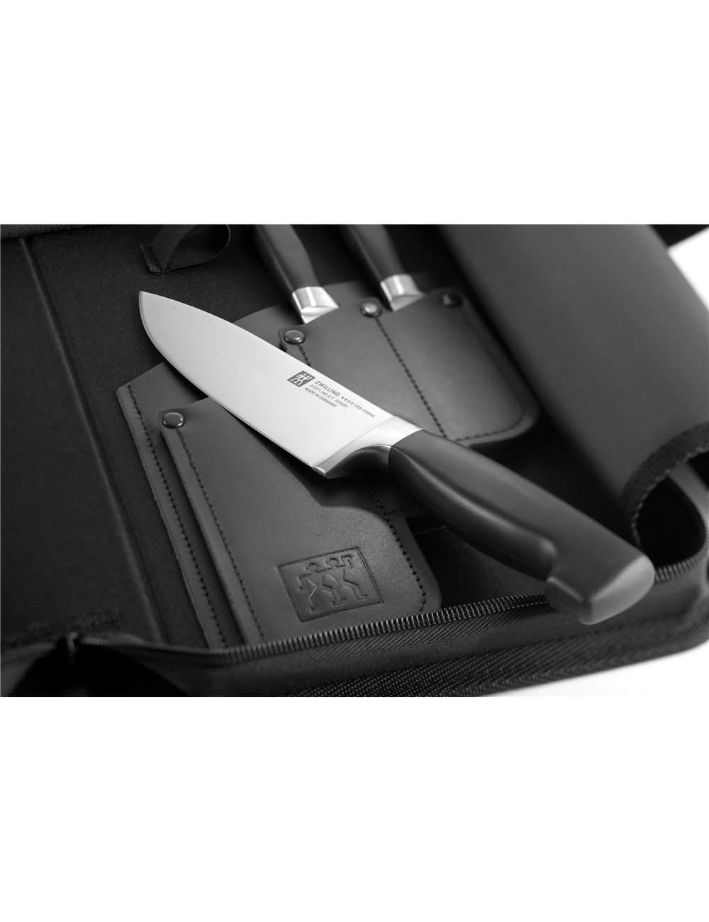 Zbliżenie noża spoczywającego na czarnym etui na noże z innymi nożami w tle.