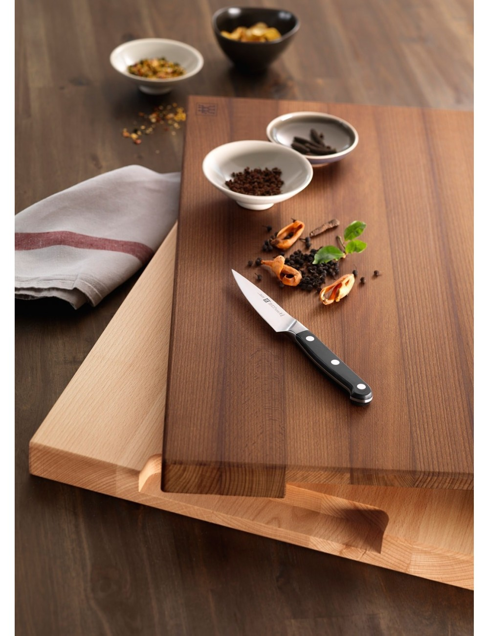 Deska do krojenia z nożem, przyprawami i małymi miseczkami. Składniki takie jak ziarna pieprzu i inne przyprawy są rozrzucone.