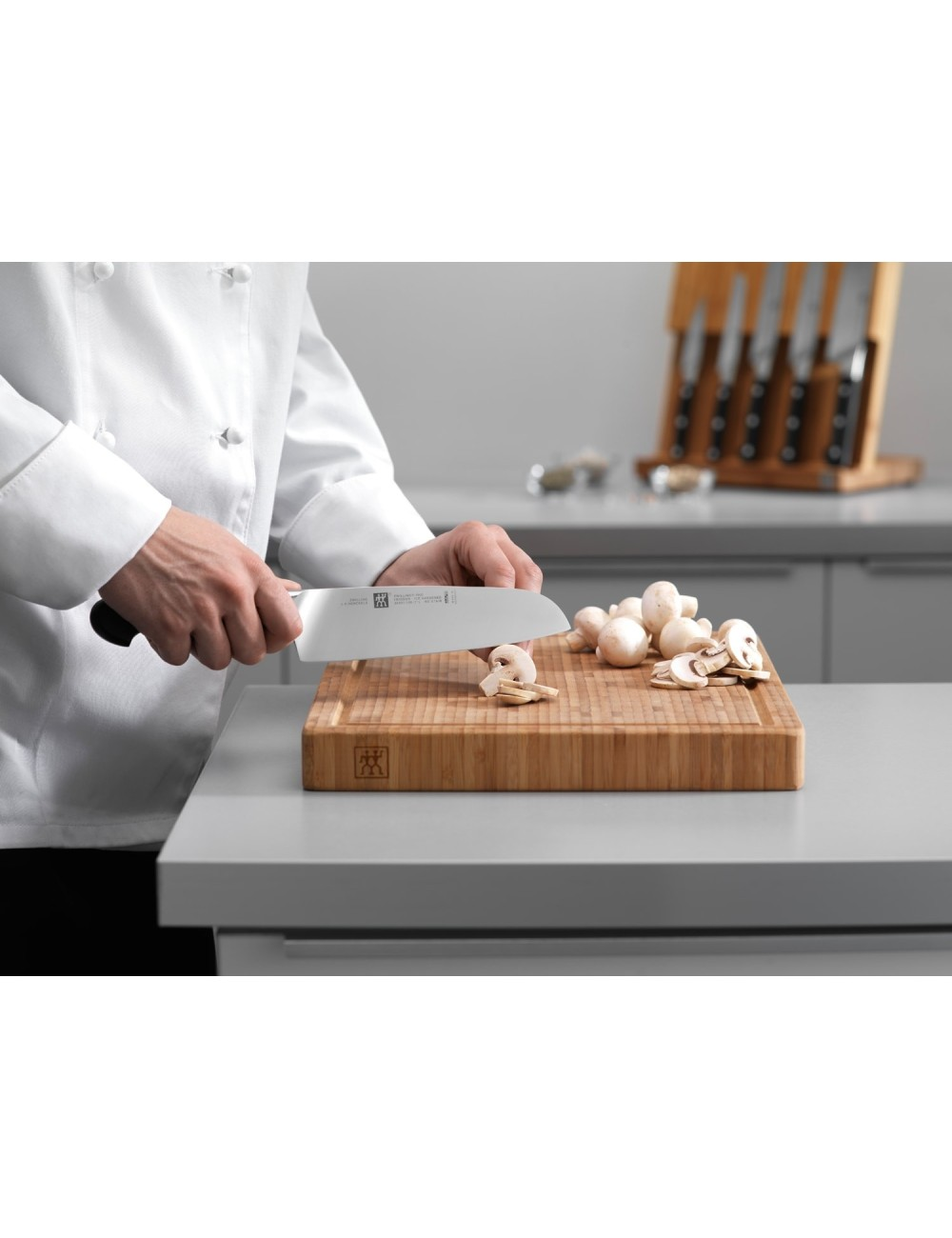 Szef kuchni kroi pieczarki na drewnianej desce do krojenia dużym nożem. Widoczne są pokrojone i całe pieczarki.