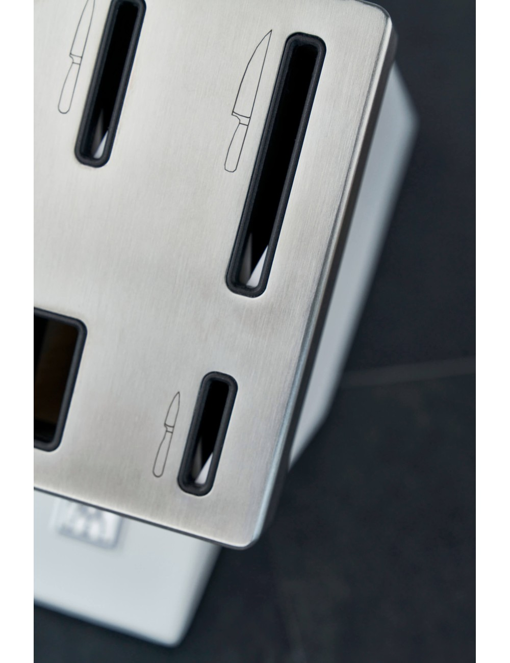 Zbliżenie na blok noży ze stali nierdzewnej z otworami. Zarysy noży z przodu. Czarne tło.