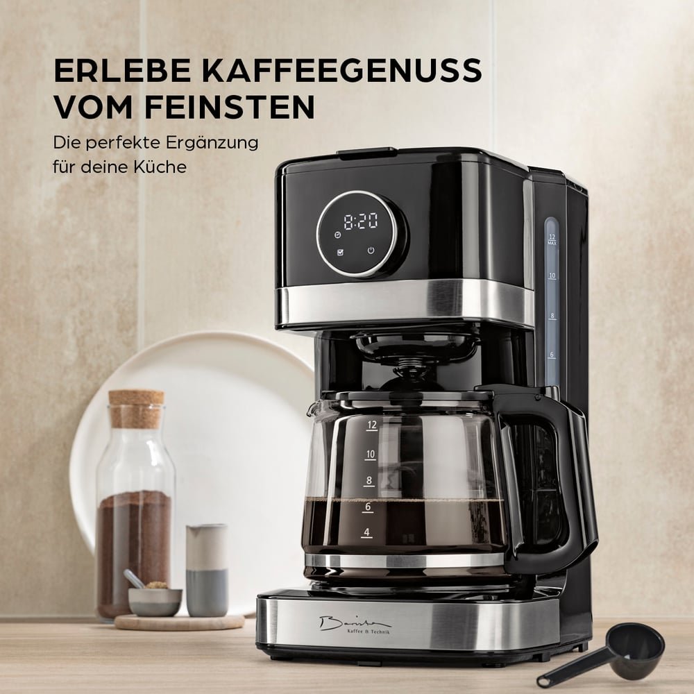 Eine schwarz-silberne Kaffeemaschine mit einer Glaskaraffe mit Kaffee steht auf einer Holzoberfläche. Weitere Gegenstände sind vorhanden.