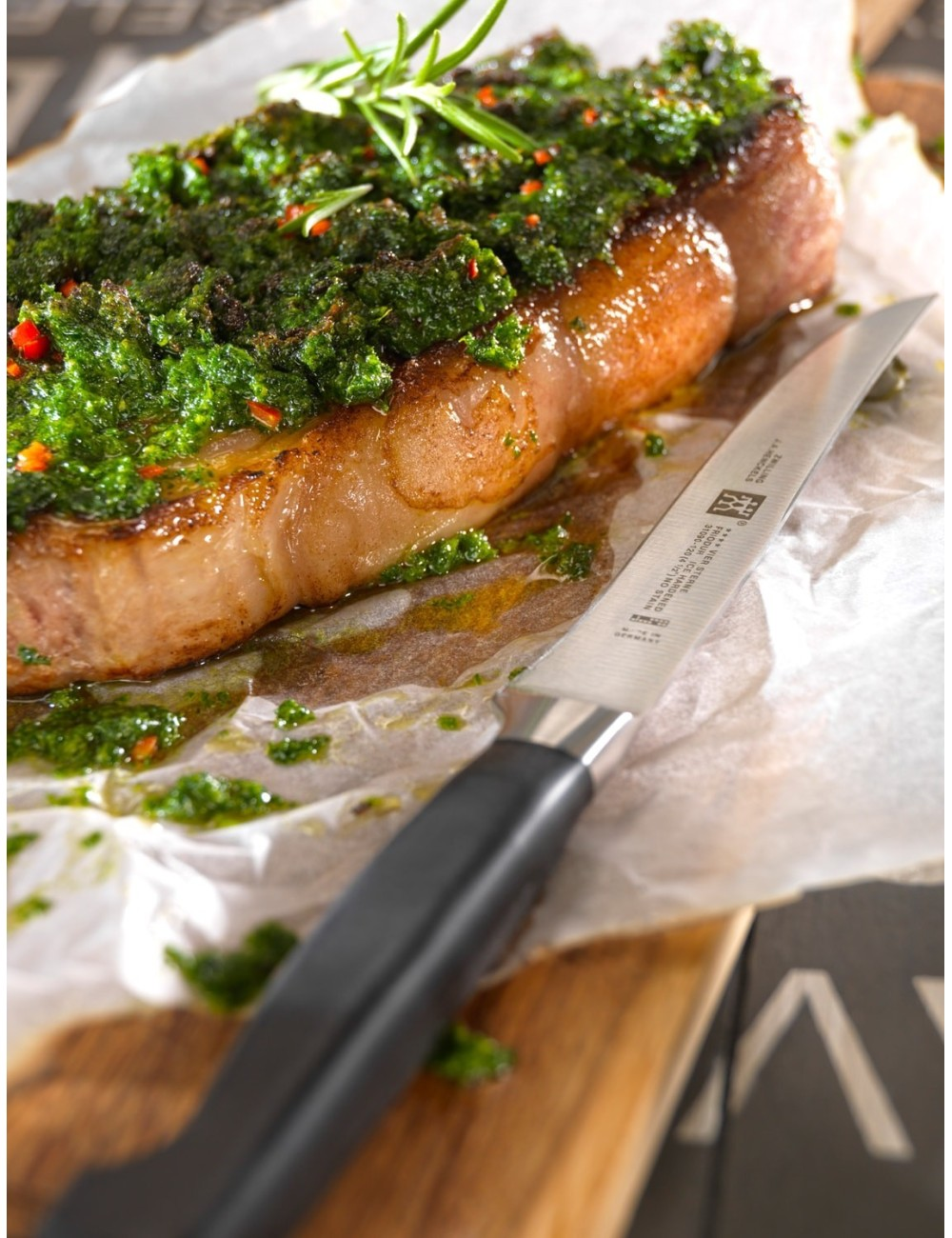 Ugotowany stek z zielonym sosem, rozmarynem i czerwoną papryką, leży na papierze z nożem obok.