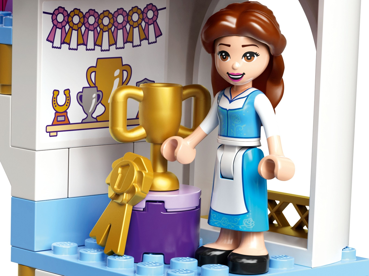 Eine Lego-Figur von Belle steht neben einer Trophäe. Ein goldenes Band und andere Trophäen sind ebenfalls zu sehen.