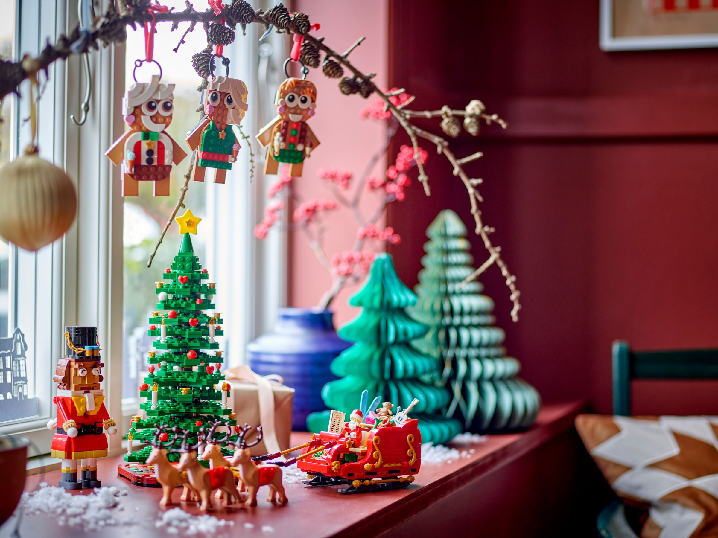 Weihnachtsdekorationen. Lego-Baum, Santa-Schlitten, hängende Lebkuchenmänner und festliche Dekoration auf einer Fensterbank.