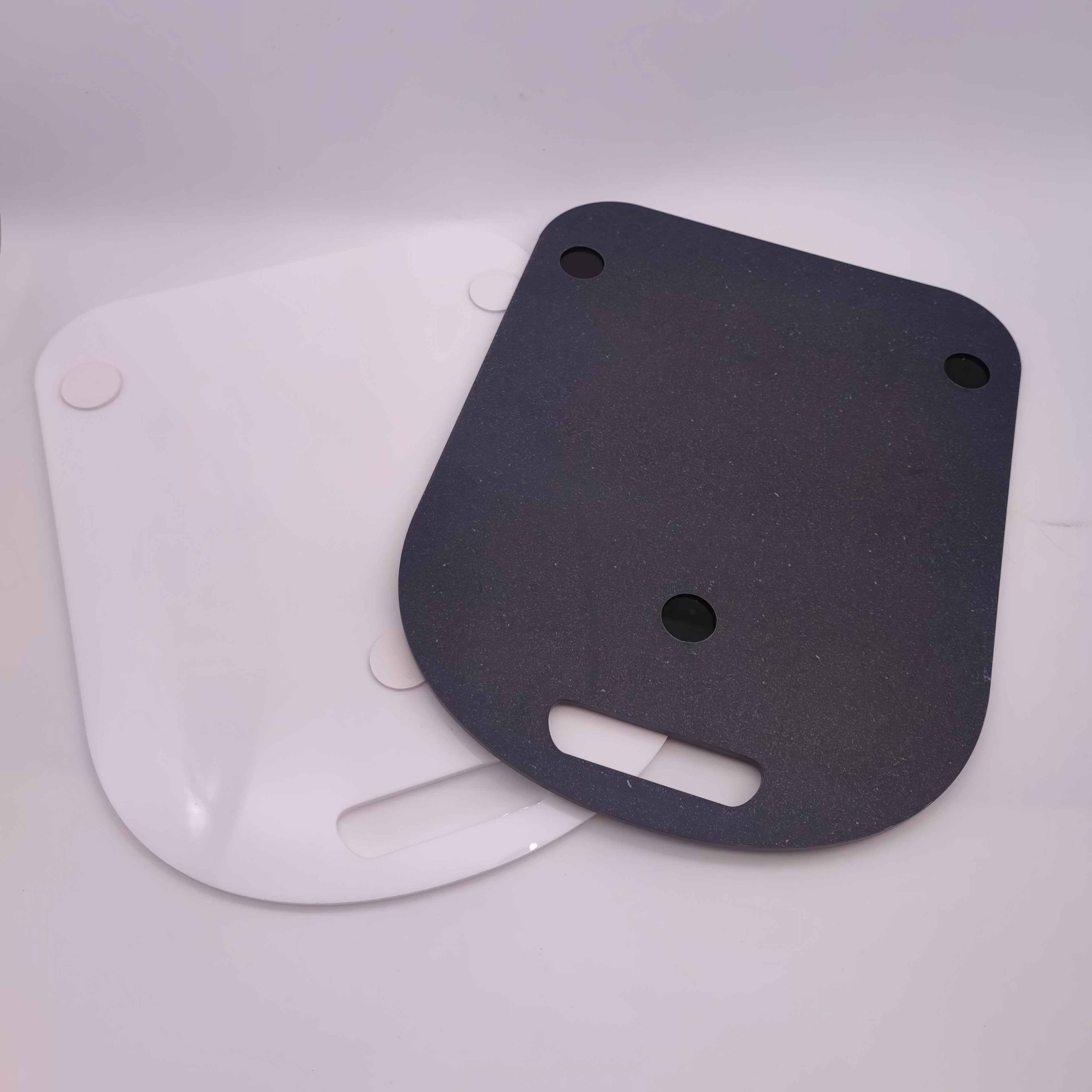 Zwei Tabletts, eines weiß und eines dunkelgrau, liegen auf einer weißen Oberfläche. Das dunkle Tablett hat Löcher und einen Griffausschnitt.