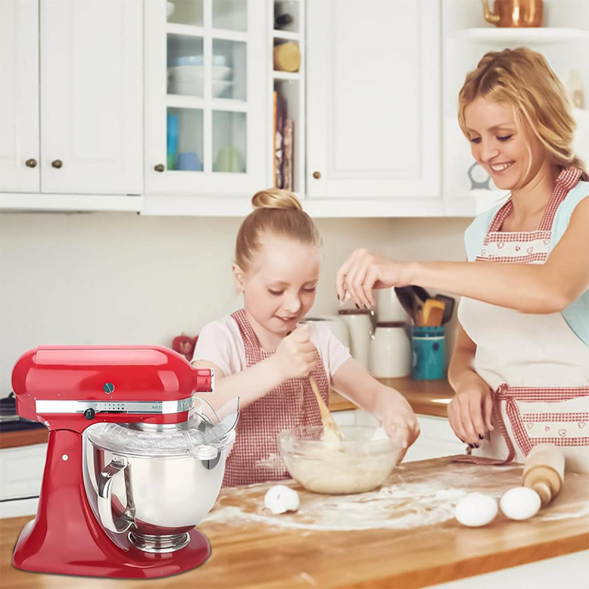 Eine Frau und ein Mädchen backen in einer Küche. Links steht ein roter Mixer. Das Mädchen verrührt Teig. Eier und eine Teigrolle liegen auf dem Tisch.