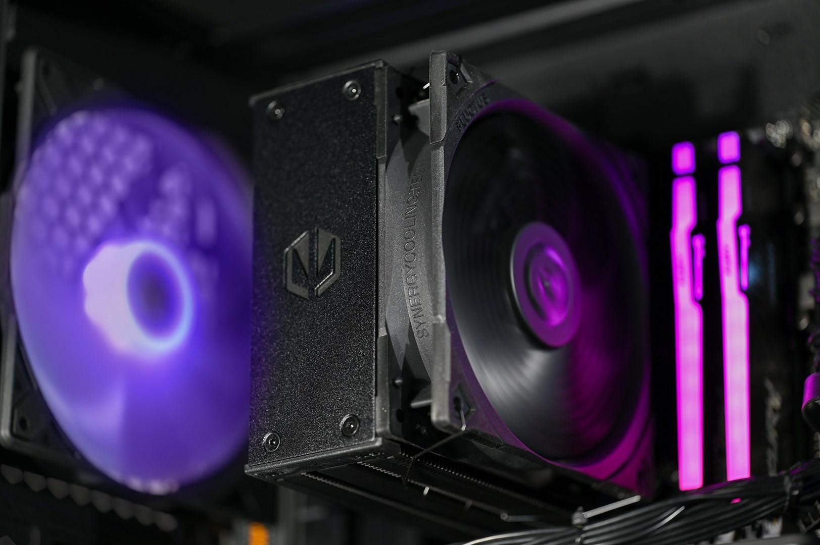 Widok wewnętrzny komputera. Pokazuje chłodnicę procesora i wentylator, oba z fioletowymi światłami. Widoczna jest również pamięć RAM z różowymi światłami.