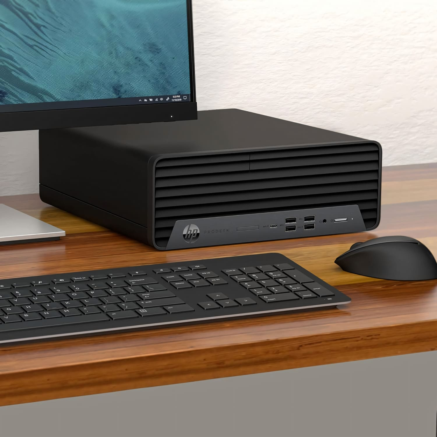 Una configuración de computadora en un escritorio de madera. Incluye una computadora de escritorio negra, monitor, teclado y mouse.
