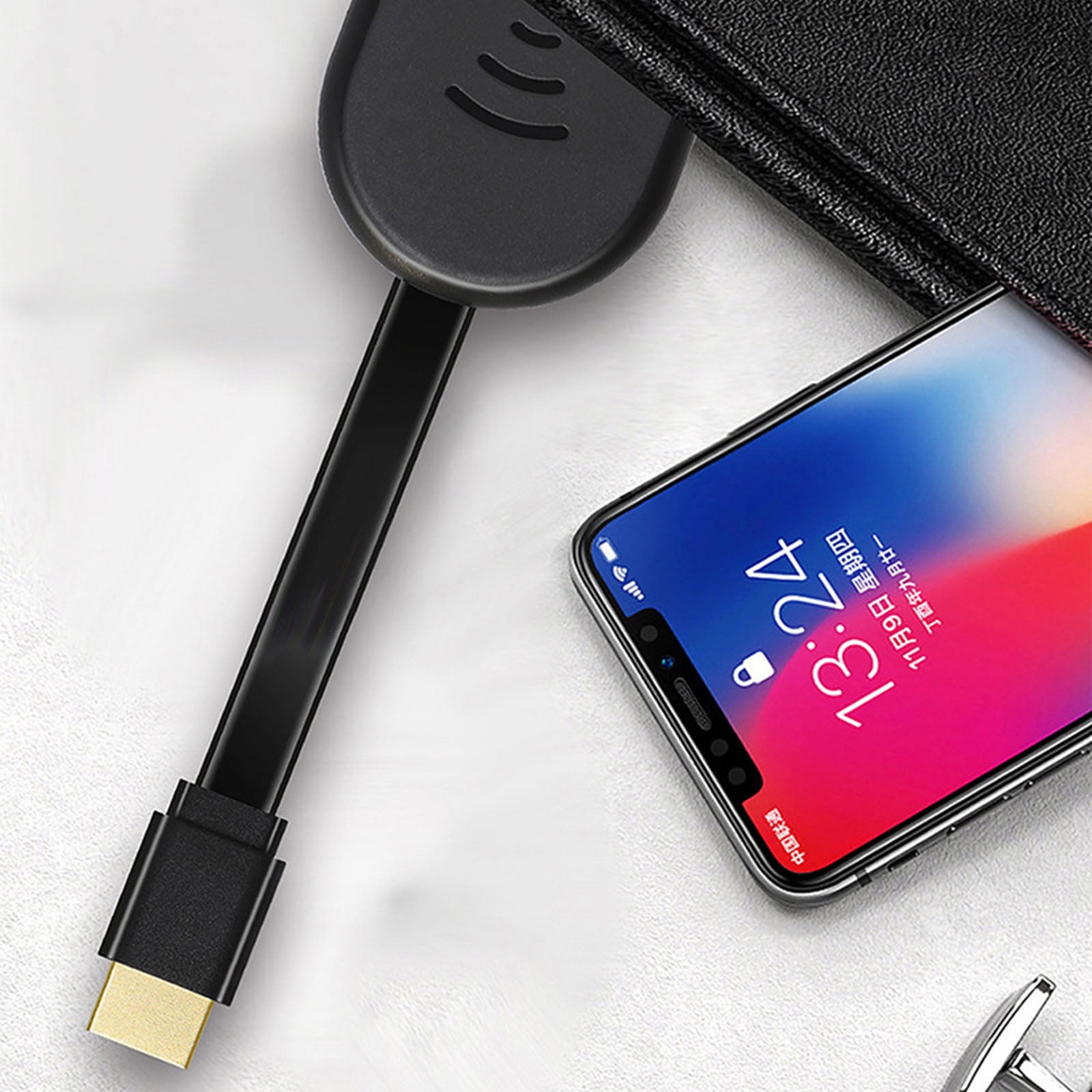 Ein Telefon mit der Anzeige 13:24, ein schwarzes Gerät und ein schwarzes Kabel mit goldfarbenem Stecker auf weißer Oberfläche.