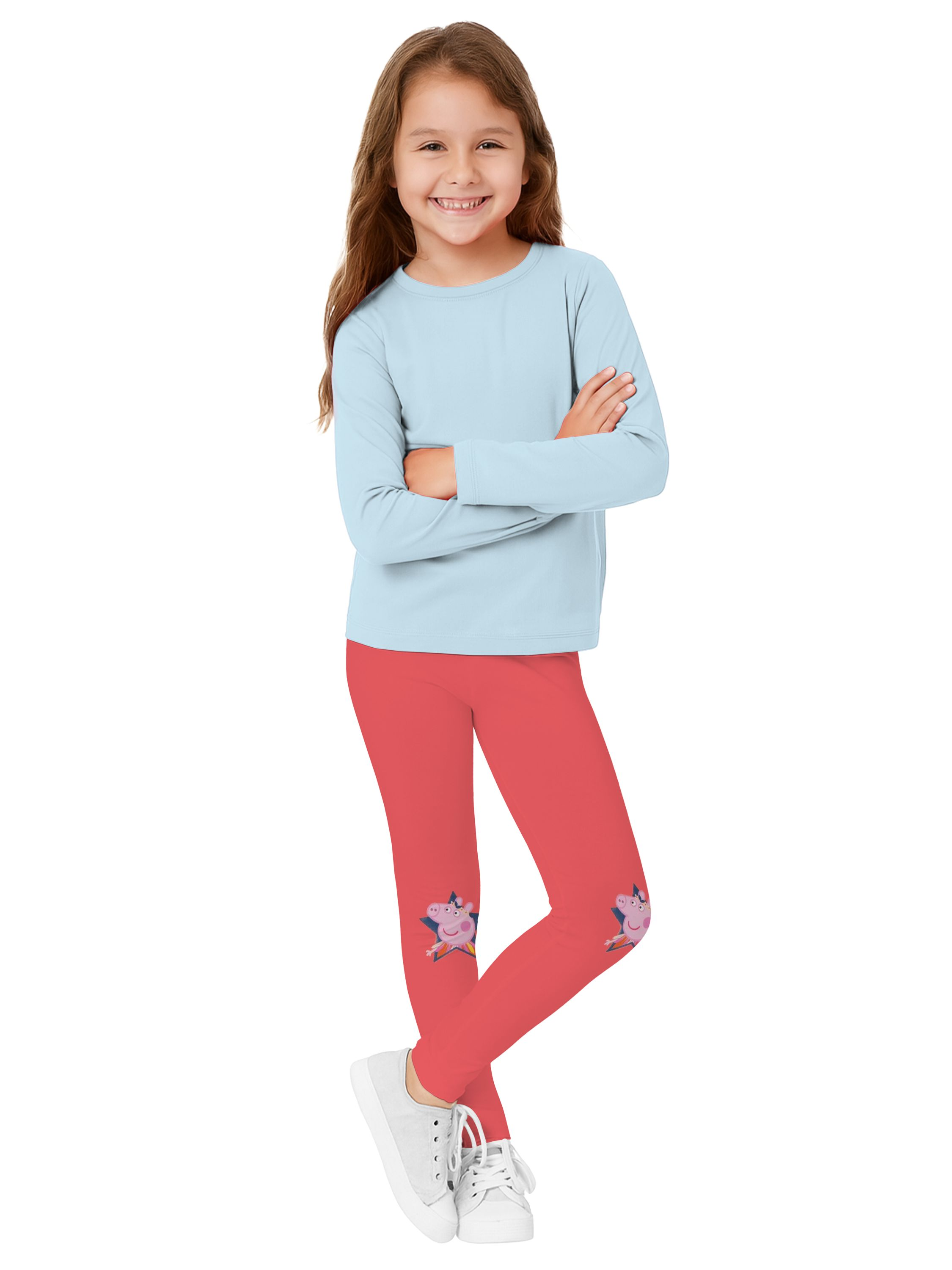 Ein lächelndes Mädchen trägt ein hellblaues Hemd, rote Leggings mit Schweinefiguren und weiße Turnschuhe.