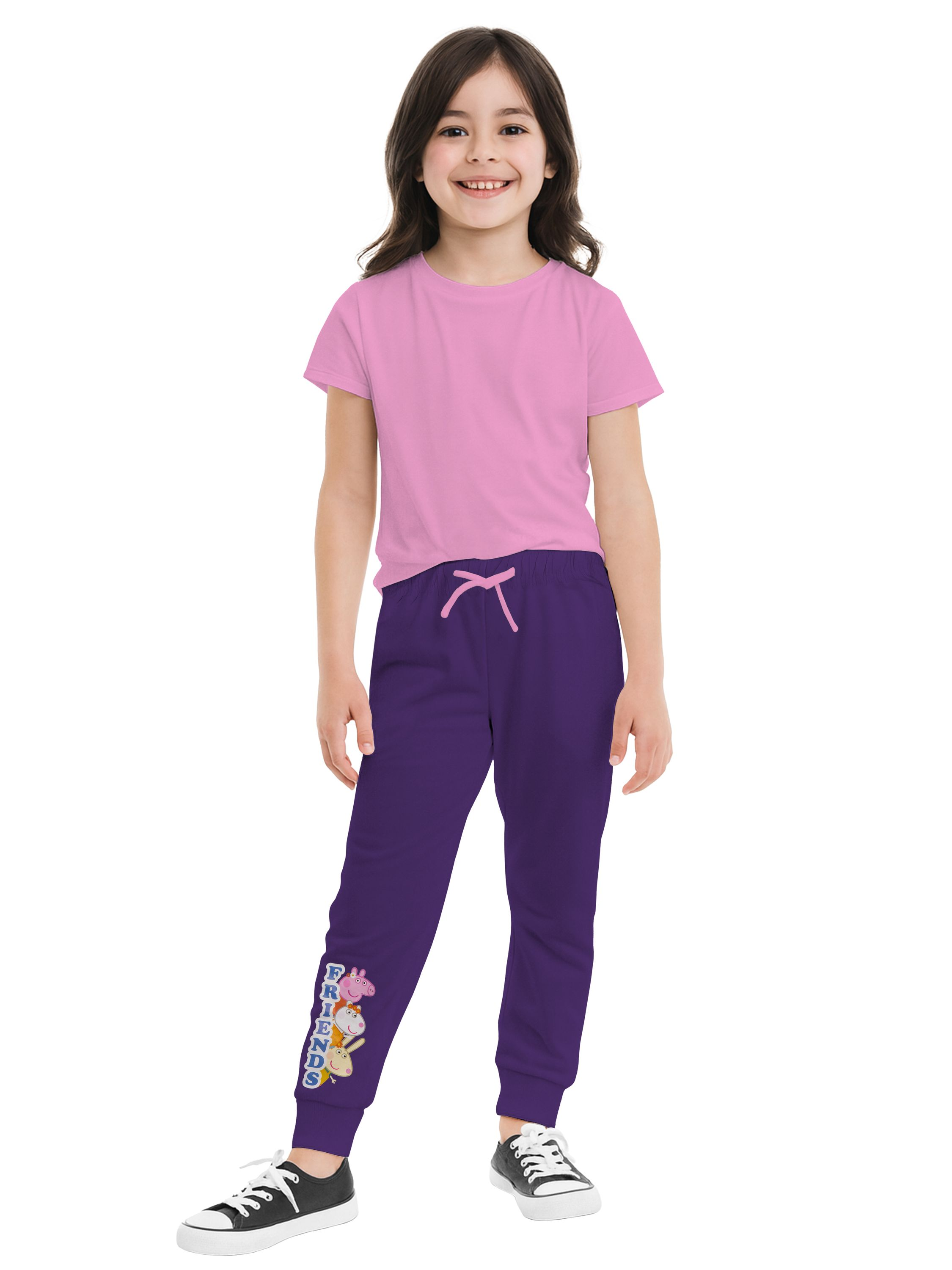 Ein lächelndes Mädchen trägt ein rosa Hemd, eine lila Hose mit Cartoon-Grafik und Turnschuhen. Weißer Hintergrund.