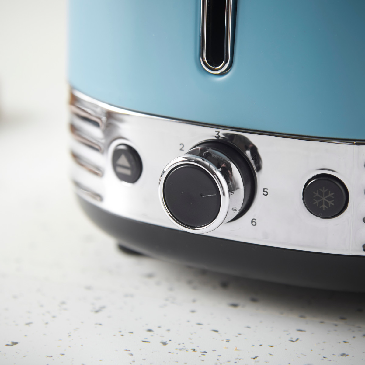 Nahaufnahme eines blauen Toasters mit Chromakzenten. Ein schwarzer Drehregler mit den Zahlen 2-6 und eine Schneeflockentaste sind sichtbar.