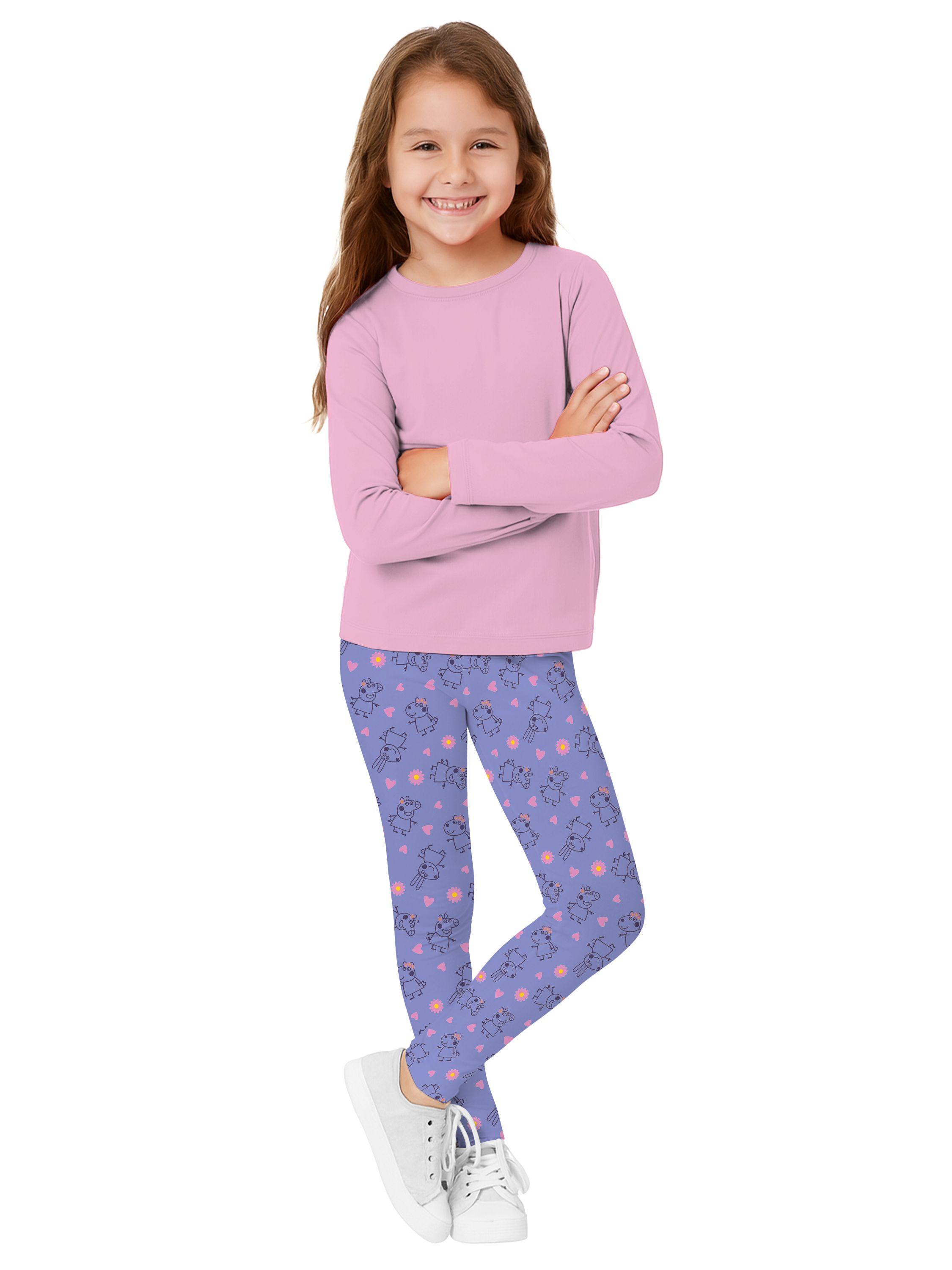 Ein lächelndes Mädchen mit langen Haaren trägt ein rosa Hemd, blaue Leggings, weiße Schuhe, Arme verschränkt.