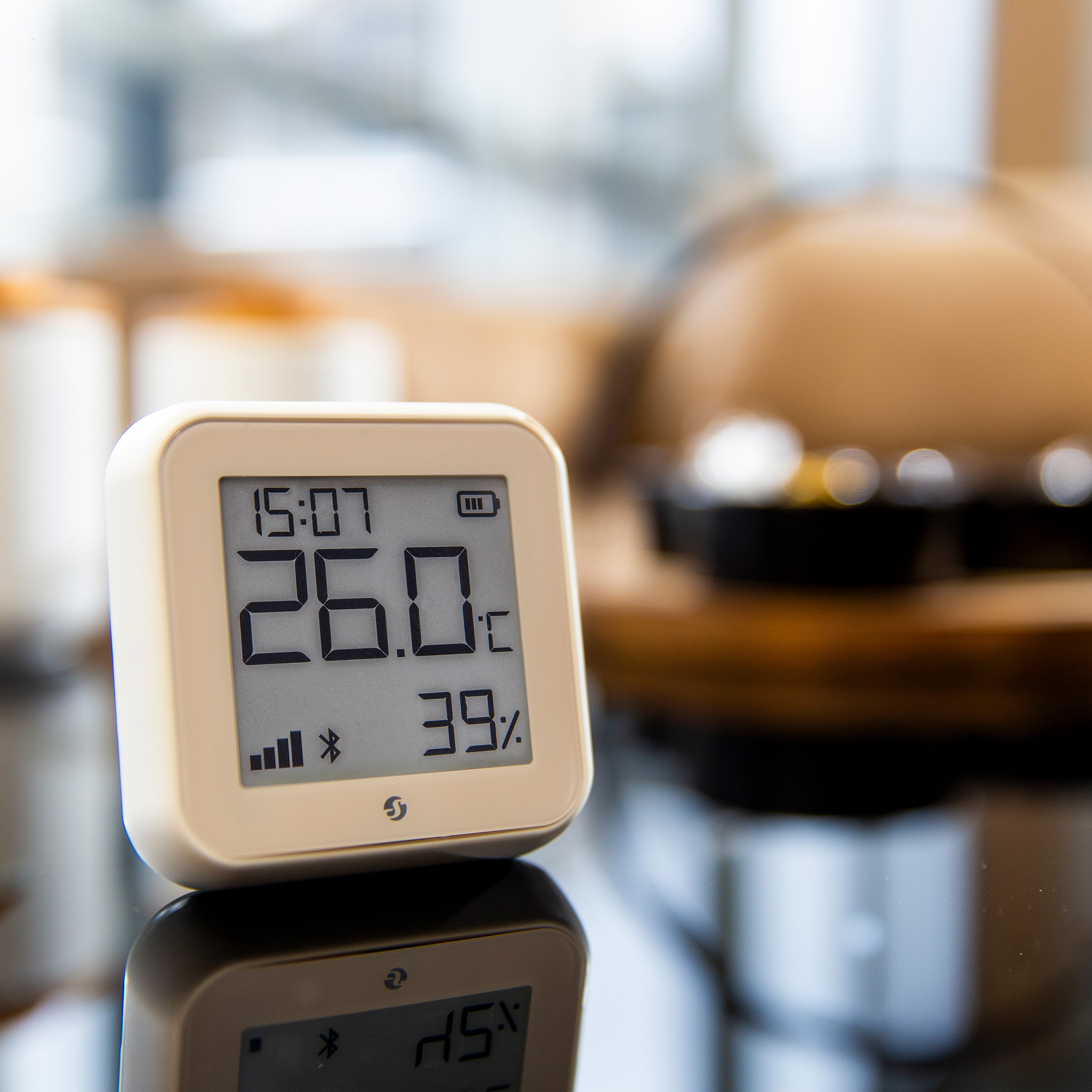 Biały termometr cyfrowy wyświetlający czas, temperaturę (26,0°C) i wilgotność (39%) na powierzchni.