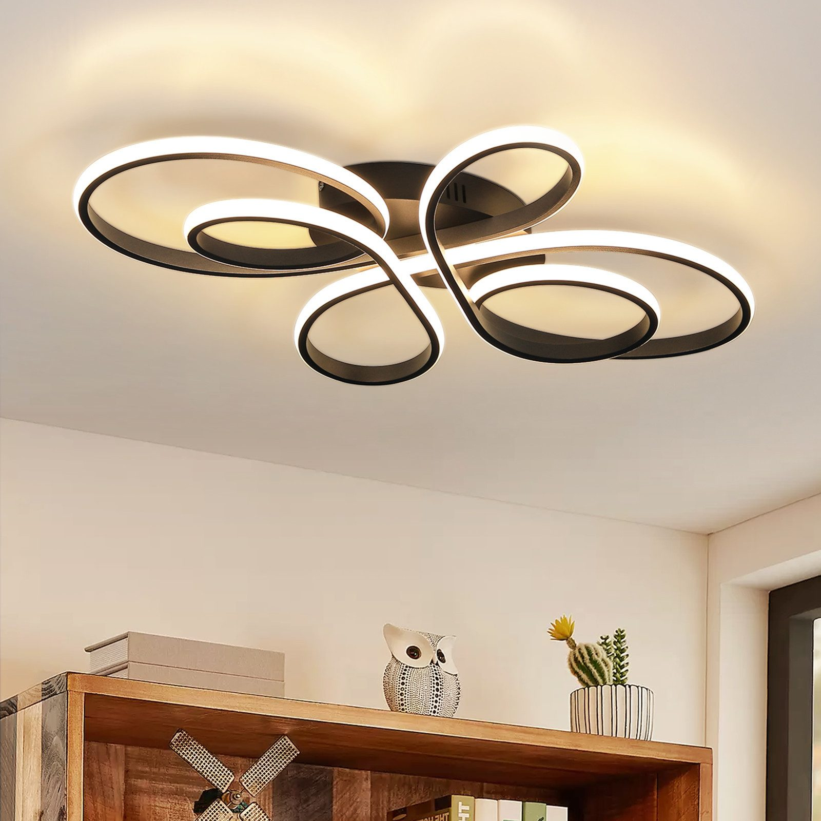 Una moderna plafoniera con cornice nera e luci bianche. Un ripiano in legno contiene decorazioni. Parete bianca e angolo della stanza.