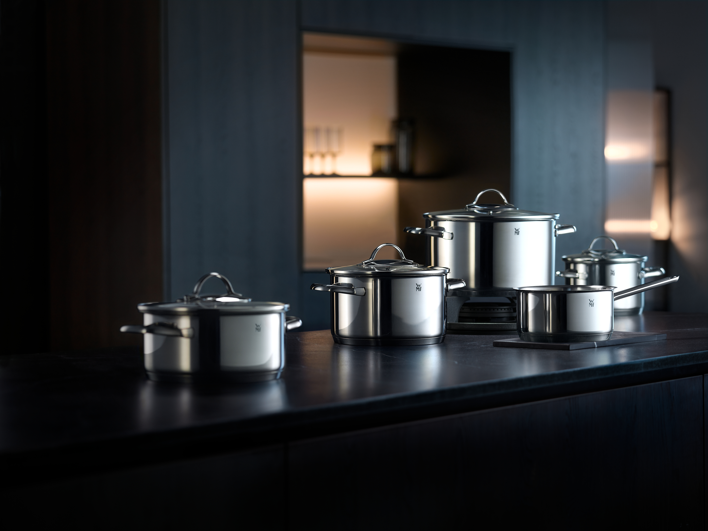 Casseroles et poêles en acier inoxydable sur un comptoir de cuisine sombre. Une étagère avec des bouteilles en verre à l'arrière-plan.