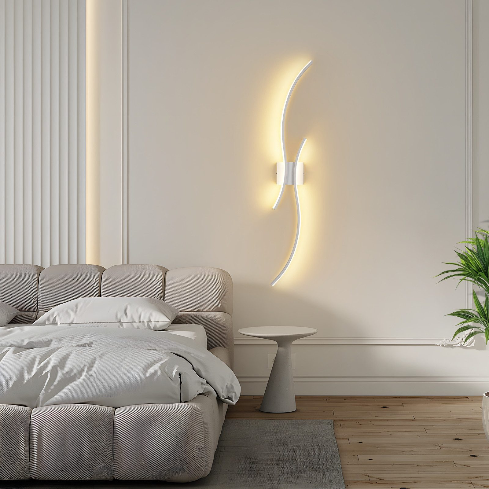 Camera da letto con letto, lampada e comodino. Dominano i toni beige. Una pianta è nell'angolo destro.