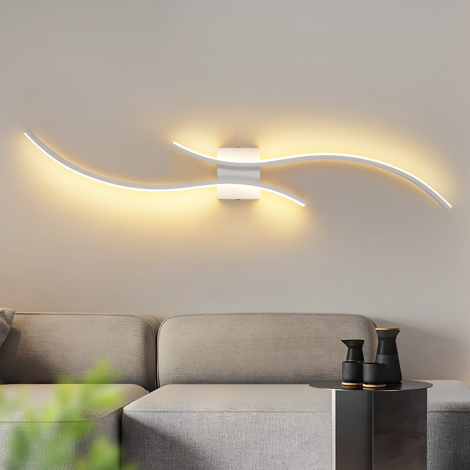 Una moderna lampada da parete con design ondulato è montata sopra un divano grigio. Arredamento nero su un tavolino.