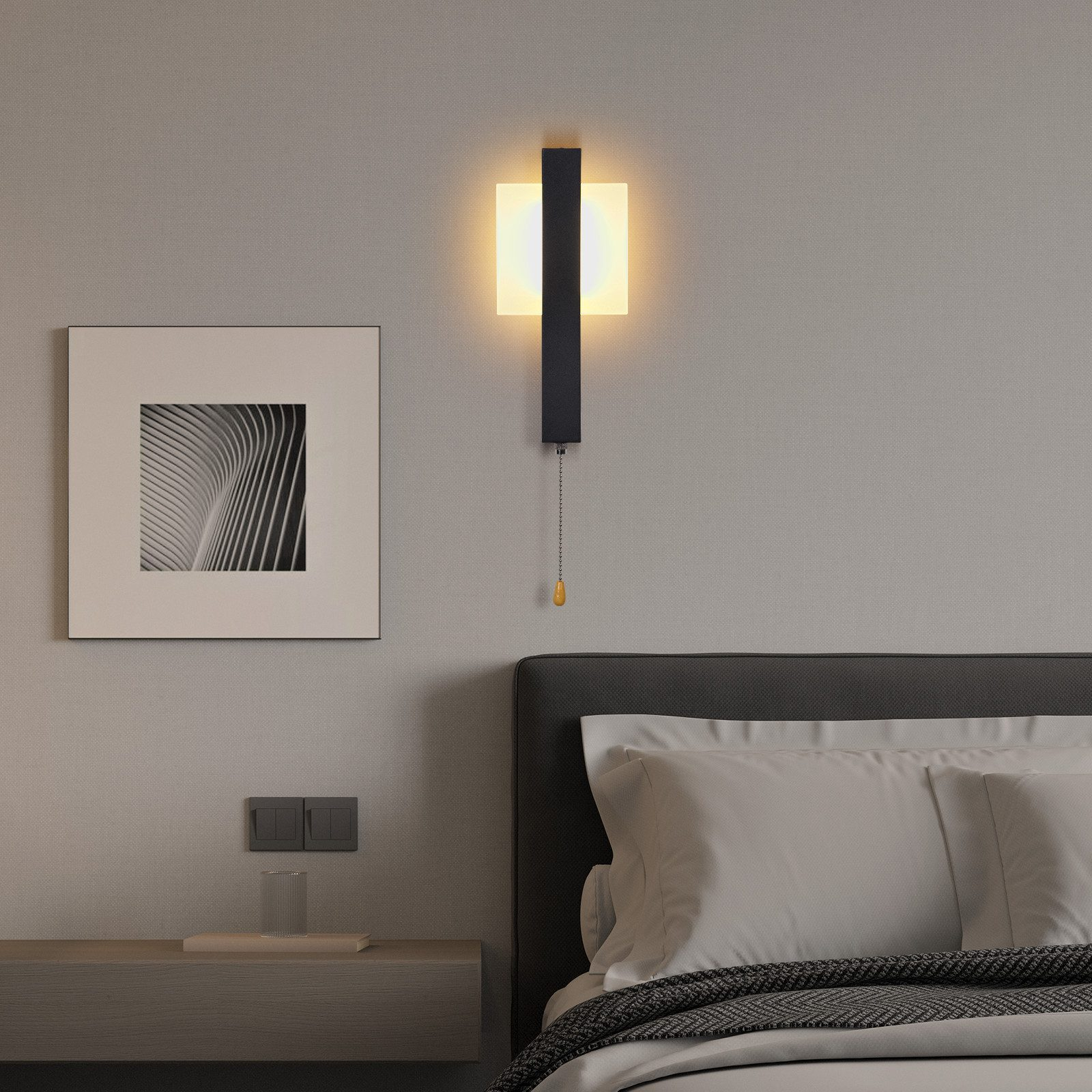 Una scena di camera da letto. Una lampada da parete illuminata, una cornice, un letto con cuscini e un comodino sono visibili.