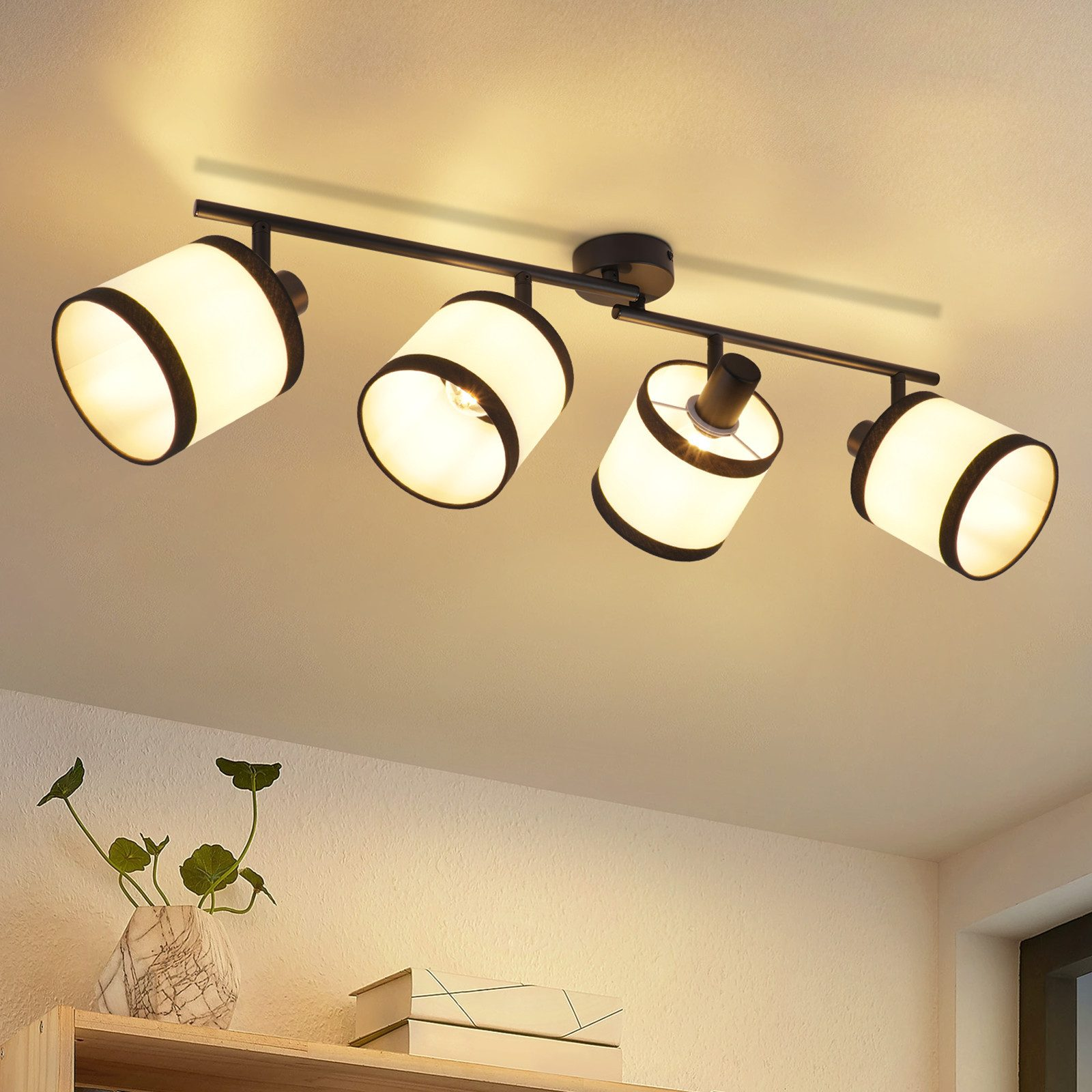 Un lampadario a soffitto con quattro lampade. Un vaso con una pianta su uno scaffale è visibile in primo piano.