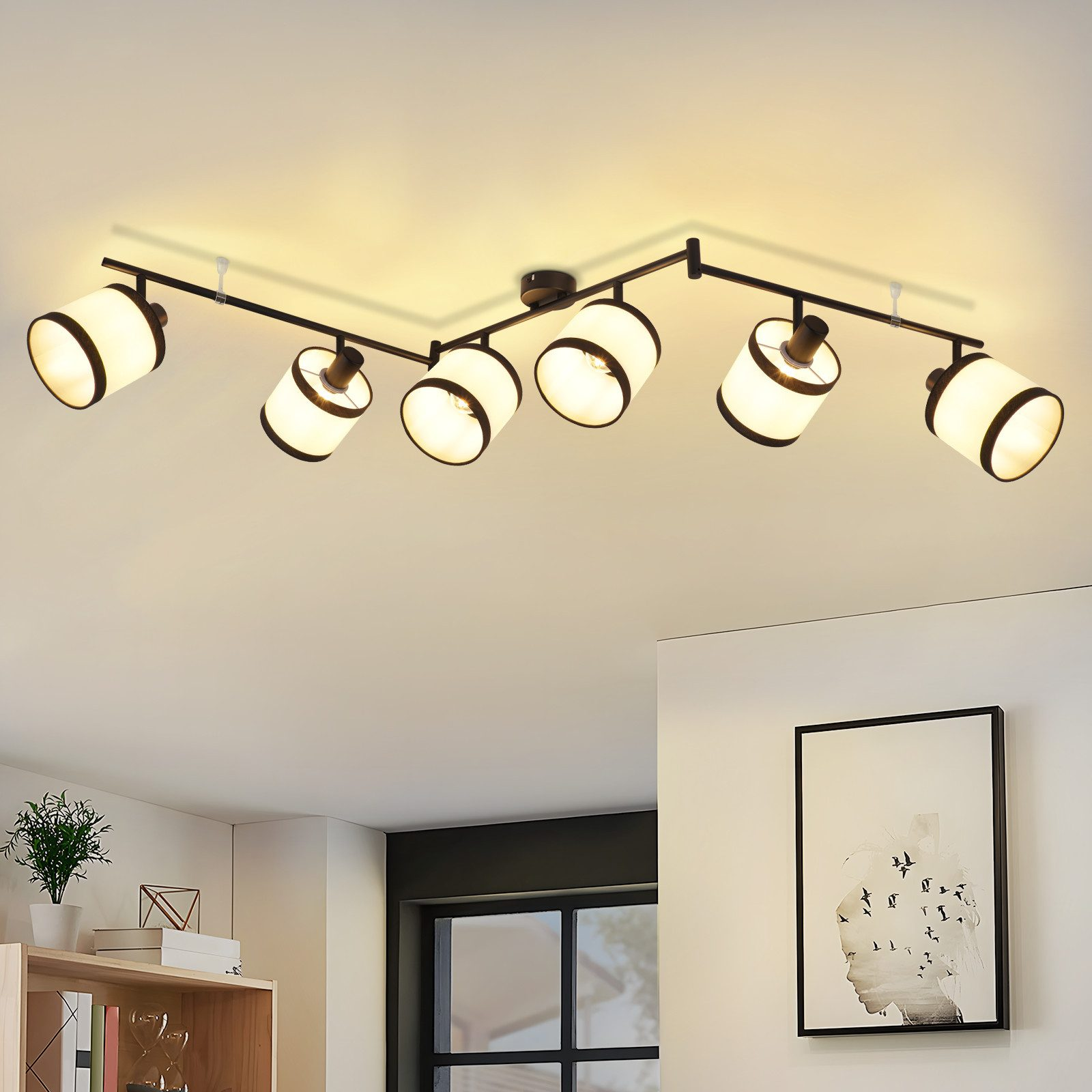 Deckenstrahler in einem Raum. Schwarzer Rahmen mit weißen Lampen. Kunstwerk an der Wand und ein Bücherregal mit Pflanzen.