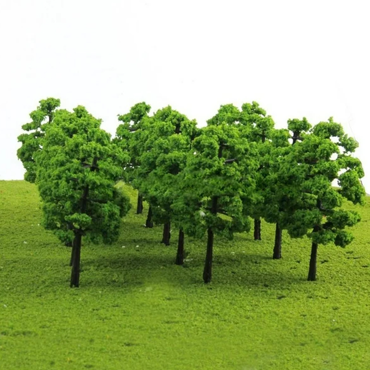 Eine Gruppe von Miniaturbäumen mit grünen Blättern und braunen Stämmen steht auf einer grünen, grasbewachsenen Oberfläche. Der Hintergrund ist weiß.