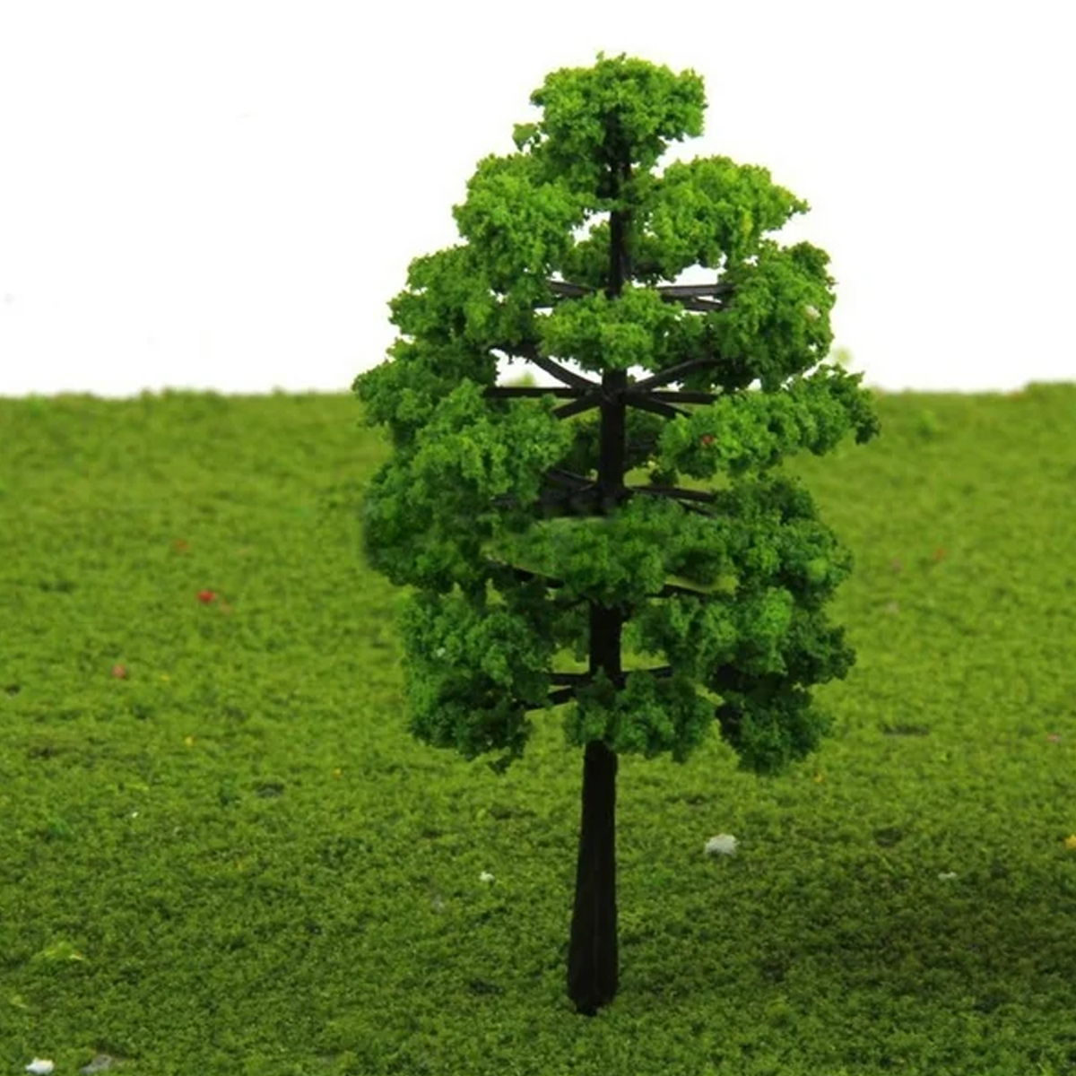 Ein Miniaturbaum mit grünem Laub und einem dunklen Stamm steht auf einer grünen, strukturierten Oberfläche. Der Hintergrund ist weiß.