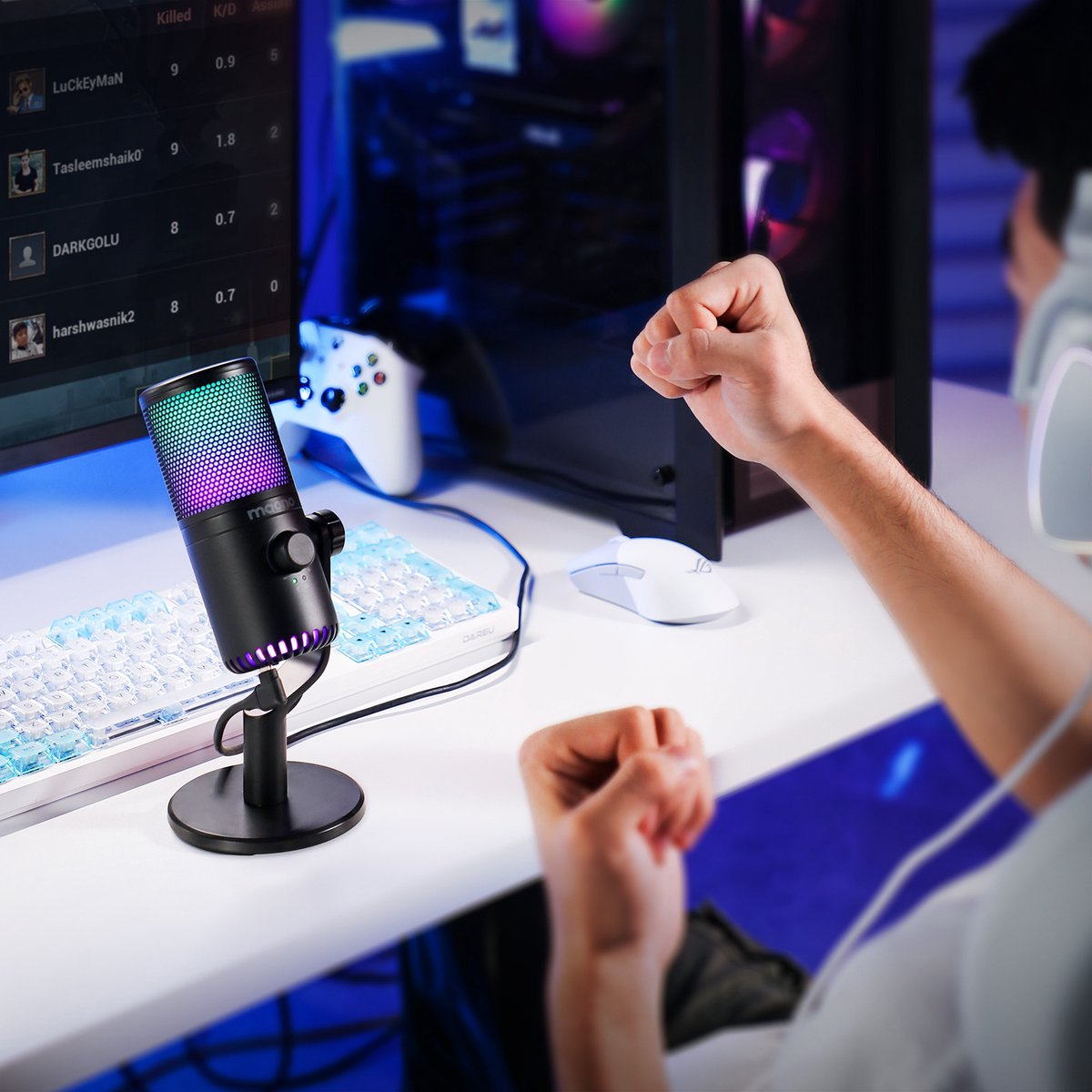 Een gaming-opstelling met een microfoon, toetsenbord, computer en een persoon die zijn vuisten balt. De microfoon heeft kleurrijke lichten.