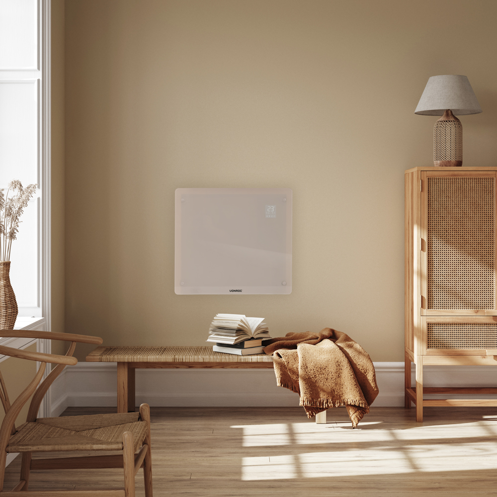 A room with a wall-mounted heater, bench with books and blanket, wooden cabinet with lamp, and a window with a chair.
