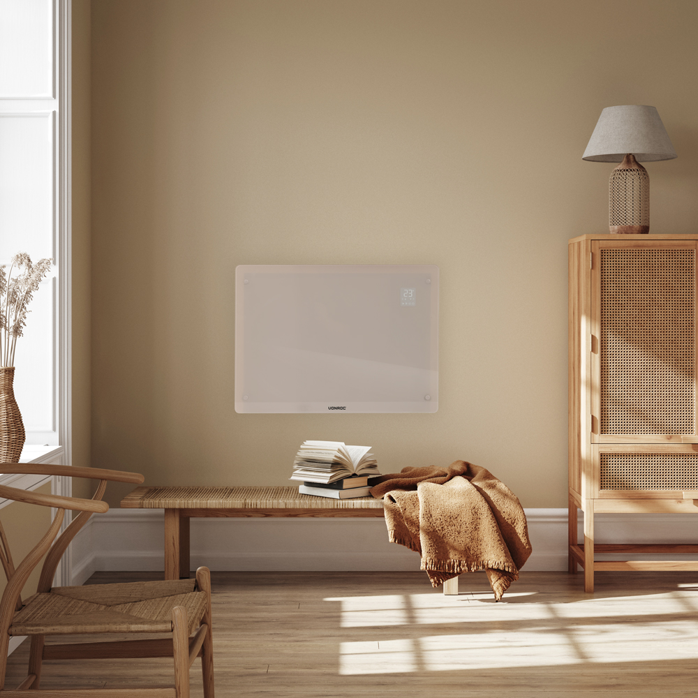 A beige wall-mounted heater above a bench with books and a blanket. A lamp and cabinet are on the right. A window is on the left.
