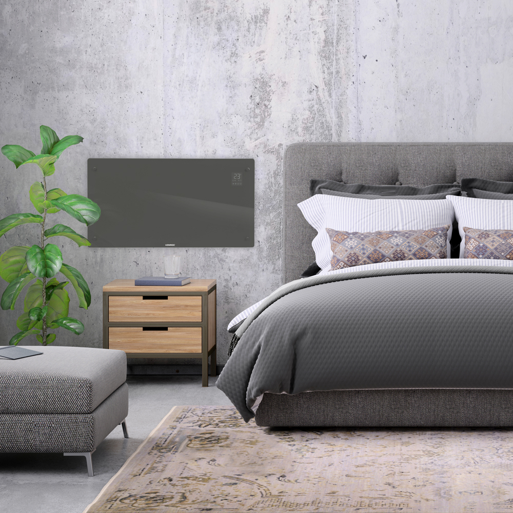 Bedroom scene with gray bed, nightstand, rug, and plant. A panel heater is on the wall. The bed has pillows and a gray comforter.