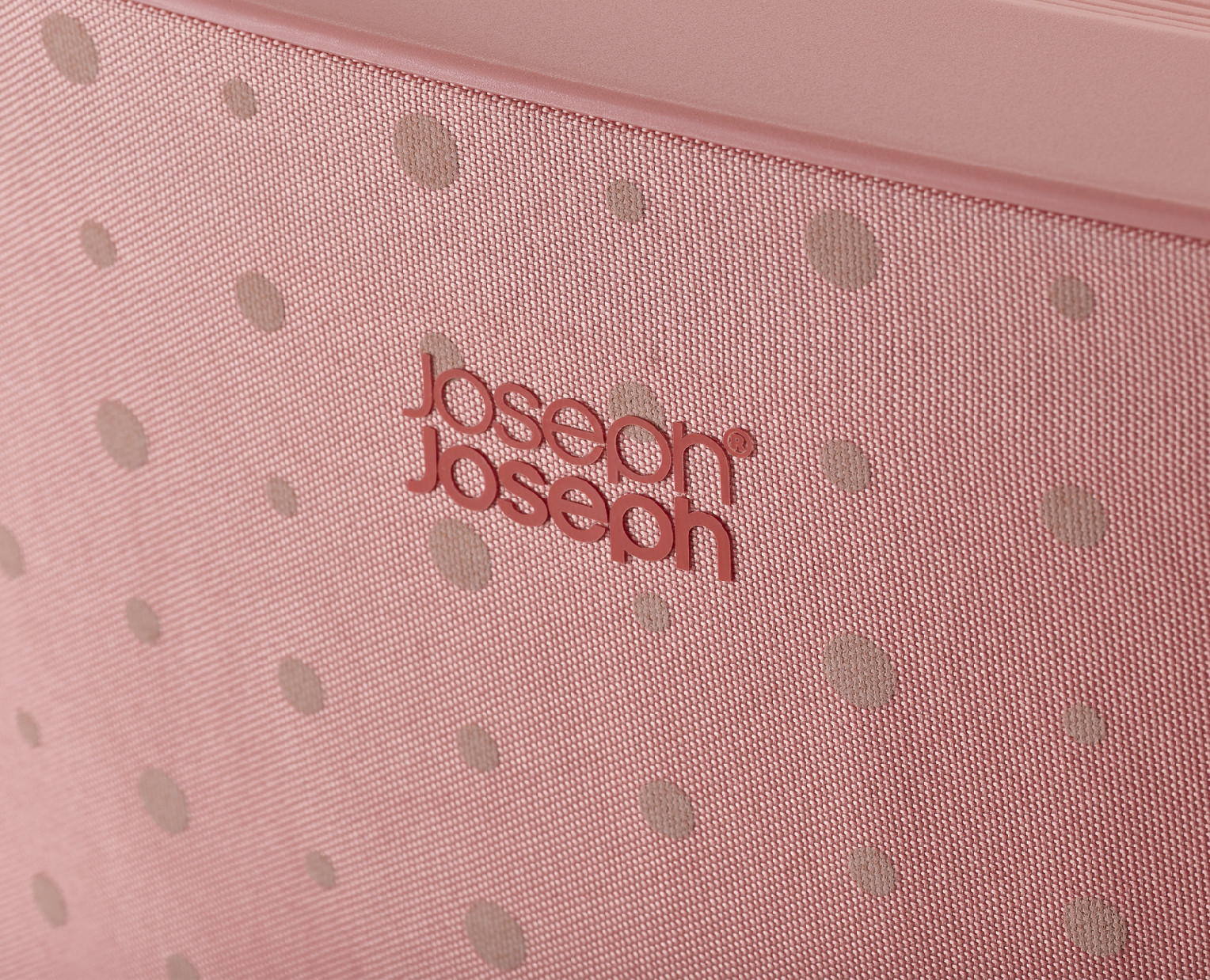 Primer plano de una maleta rosa con lunares beige. La marca 'Joseph Joseph' está grabada en rojo.